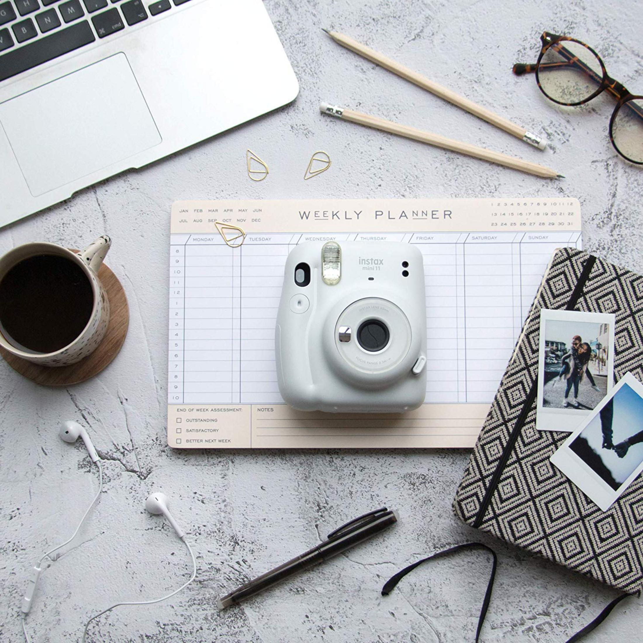 Una cámara Instax Mini 11 blanca descansa sobre un planificador semanal.
