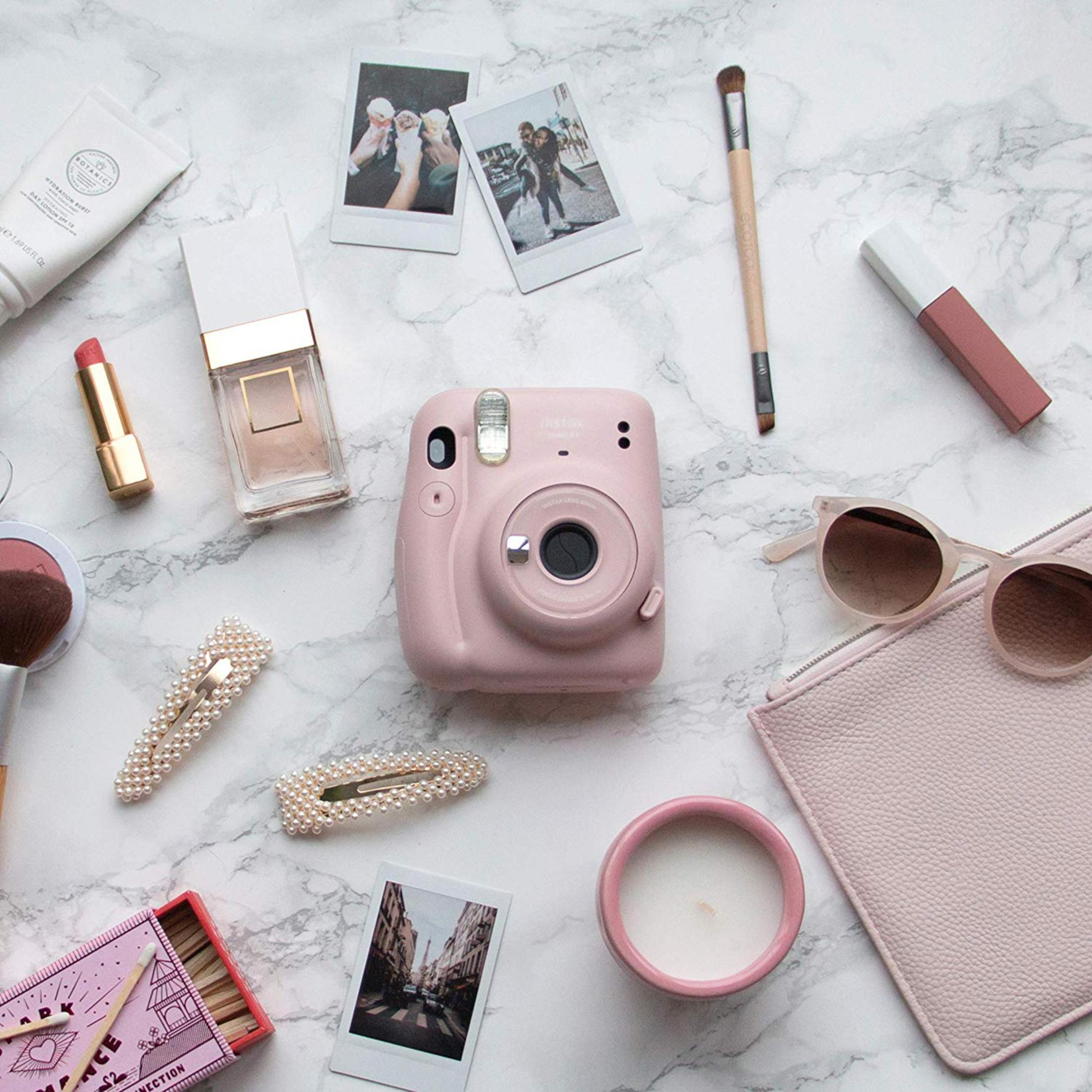 Ein rosa Instax-Kamera, Lippenstift, Parfüm, Haarklammern, Sonnenbrille, Kerze, Kamera.
