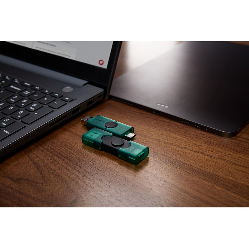 Due chiavette USB verdi su un tavolo di legno accanto a un laptop e un tablet.