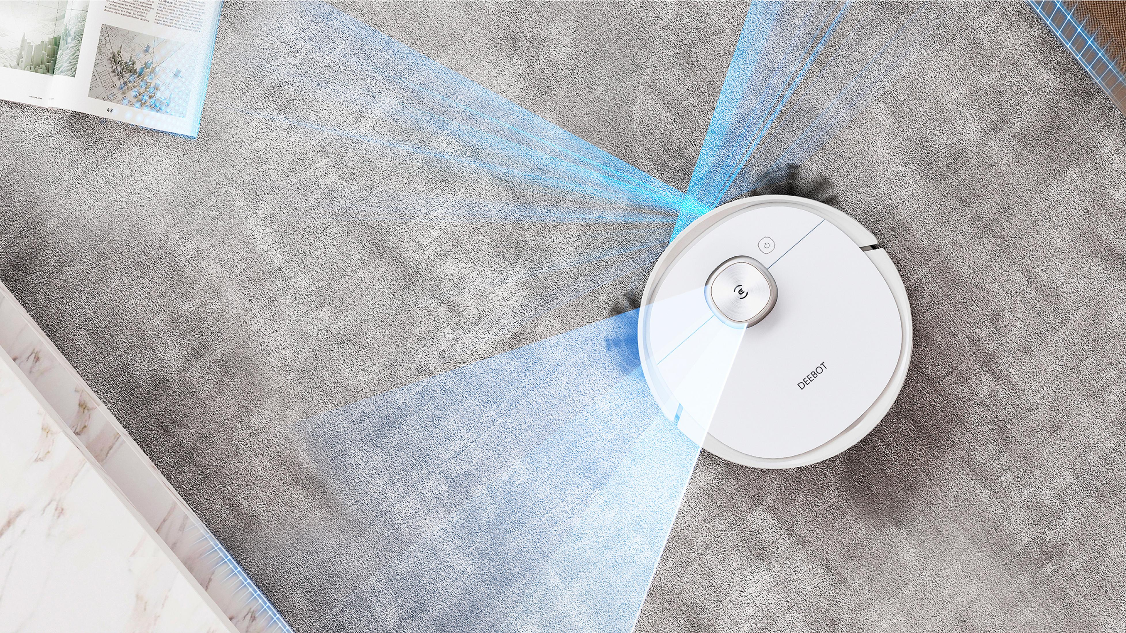 Un aspirateur robot blanc nettoie un tapis gris. Des lumières bleues indiquent son chemin.