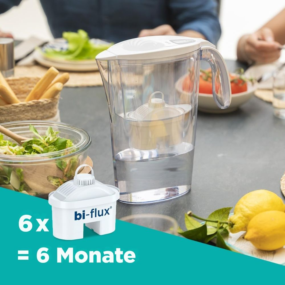 Dzbanek filtrujący wodę z sałatką, chlebem i cytrynami na stole.