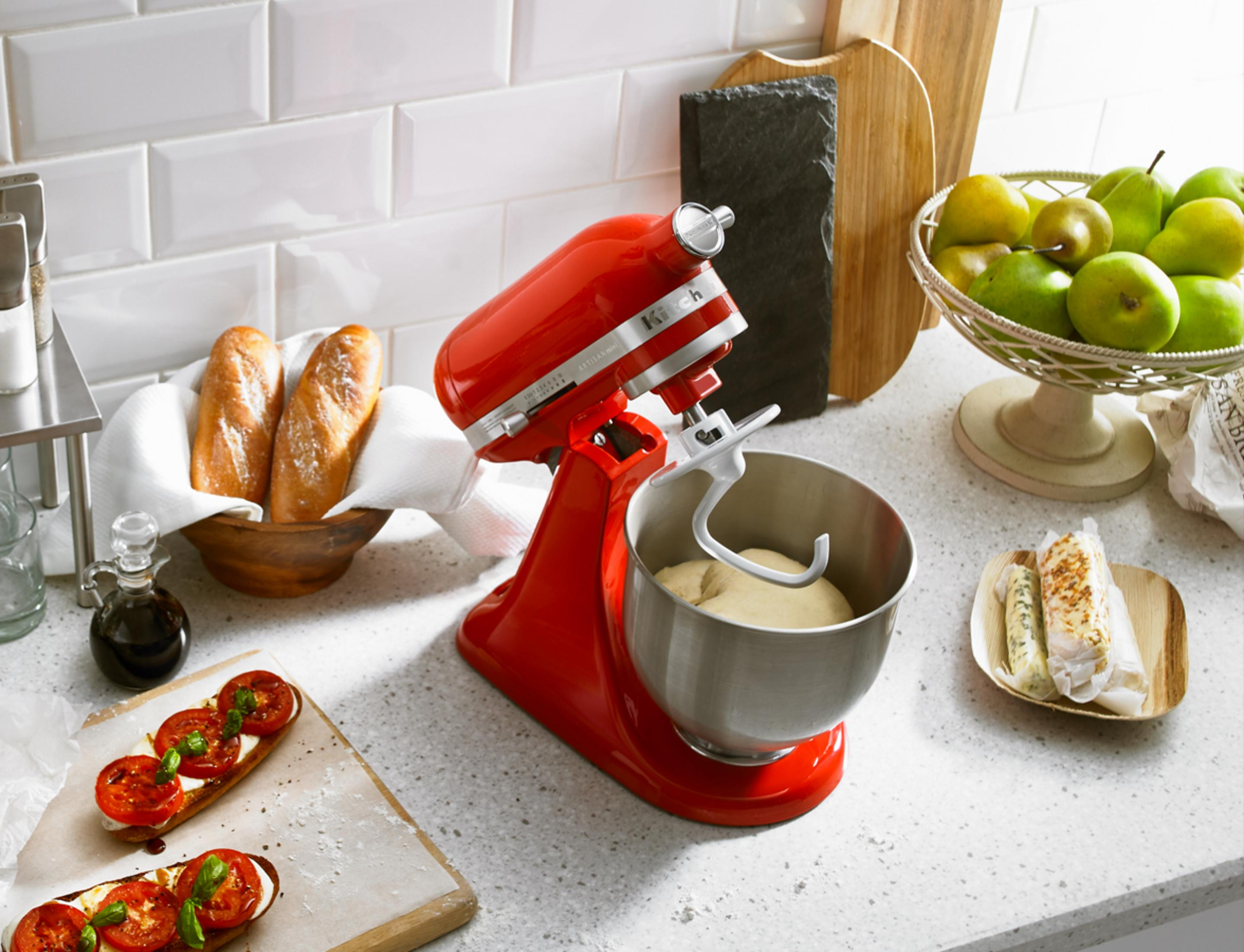 Rote Küchenmaschine mit Teig in Schüssel, Brot, Obst und Bruschetta.