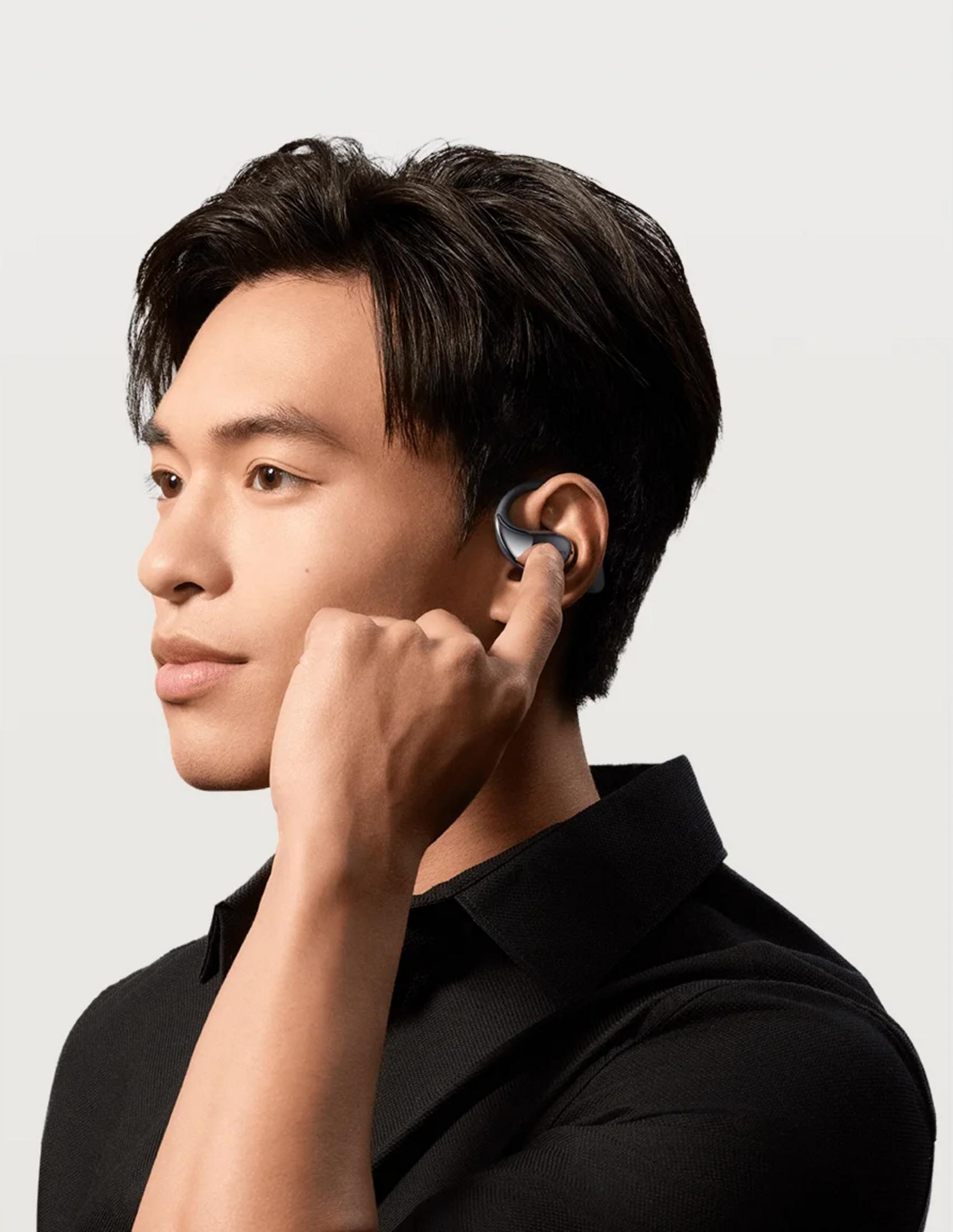 Mężczyzna z czarnymi słuchawkami w uchu, dotykający twarzy.