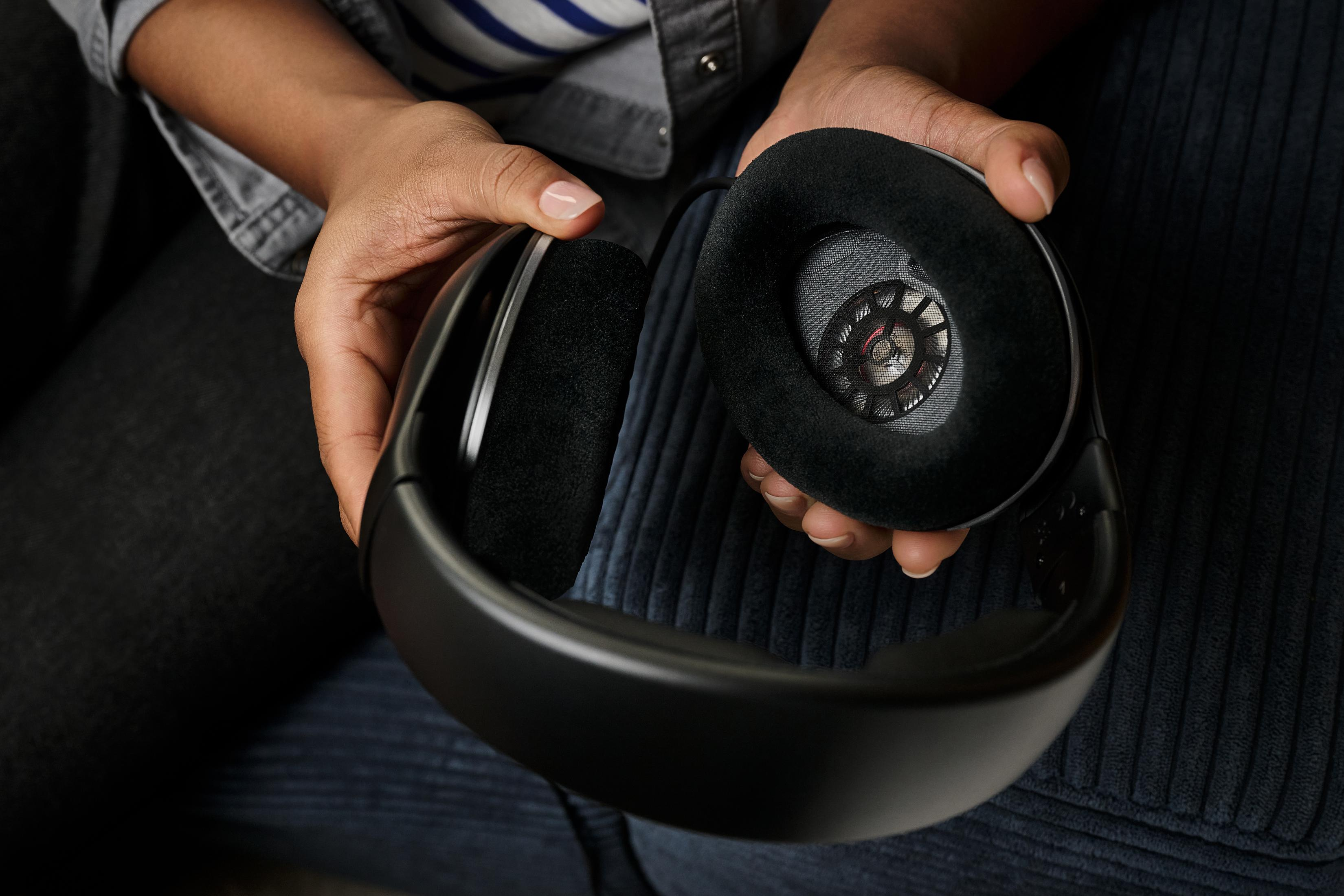 Osoba trzymająca czarne słuchawki z wyściełanymi nausznikami.