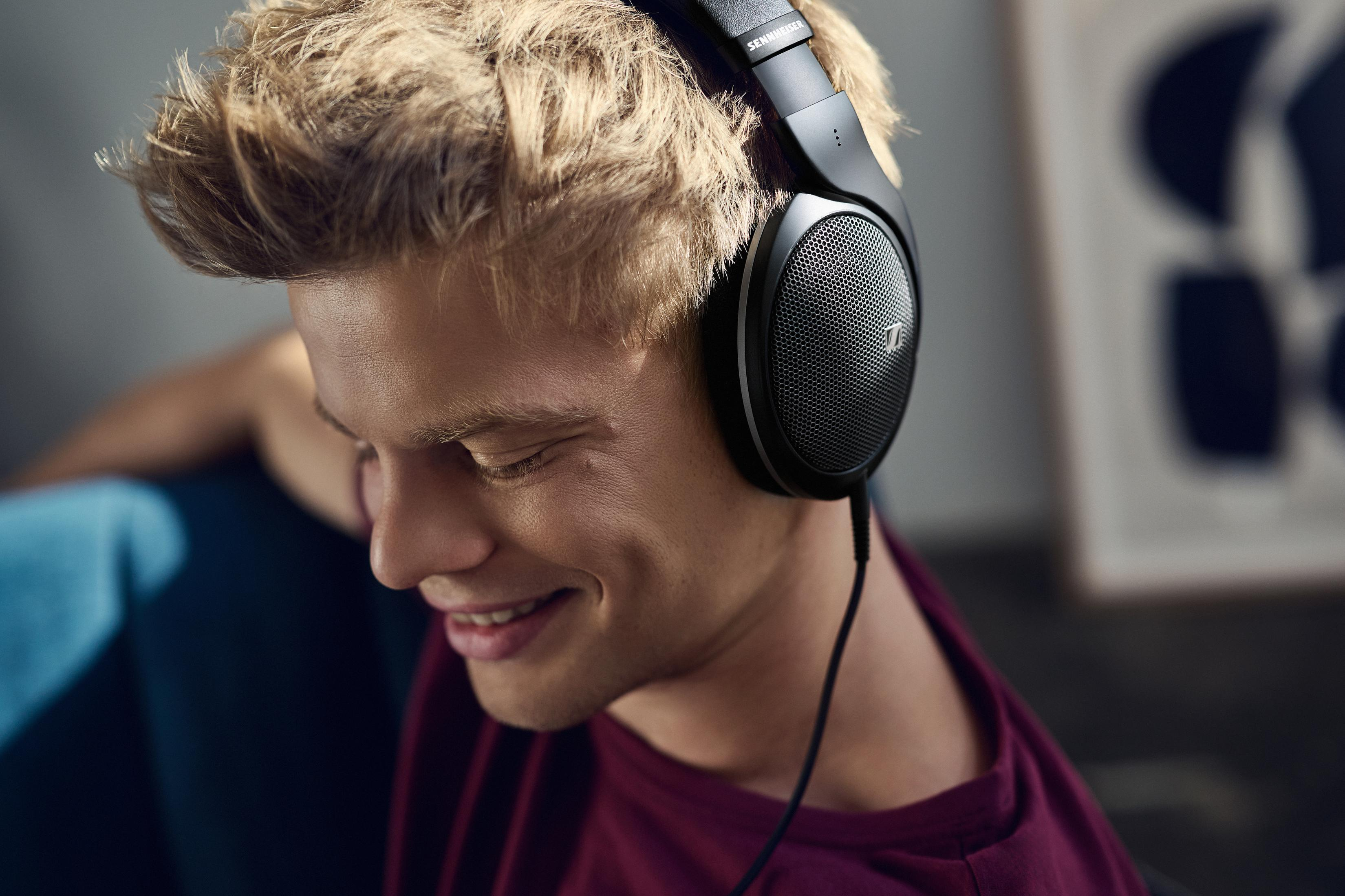 Młody blondyn ma na sobie słuchawki i uśmiecha się.