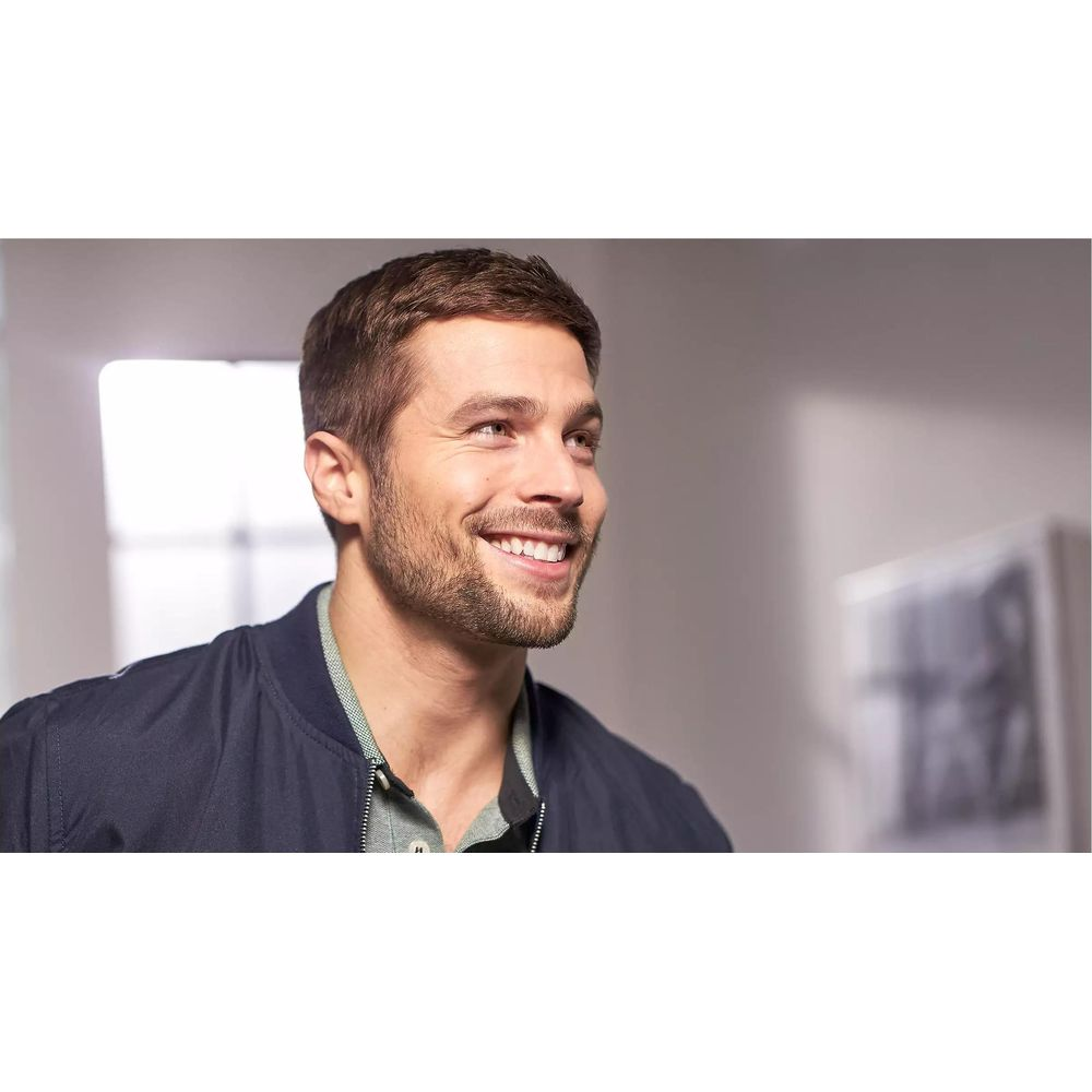 Mężczyzna z brodą uśmiecha się w prawo. Nosi ciemnoniebieską kurtkę.