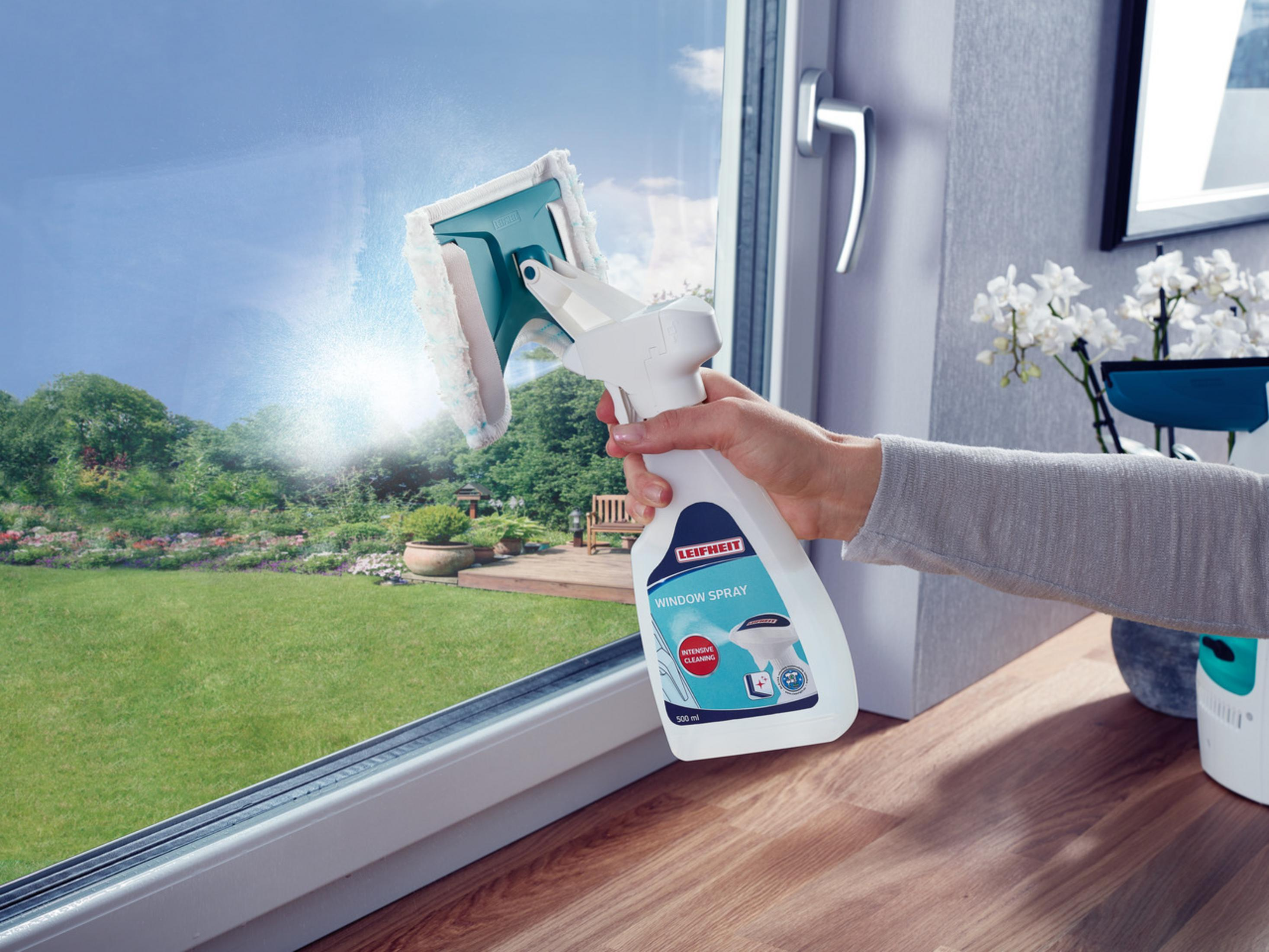 Eine Hand sprüht ein Fenster mit Leifheit Fensterreiniger und wischt es mit einem Schwamm ab.
