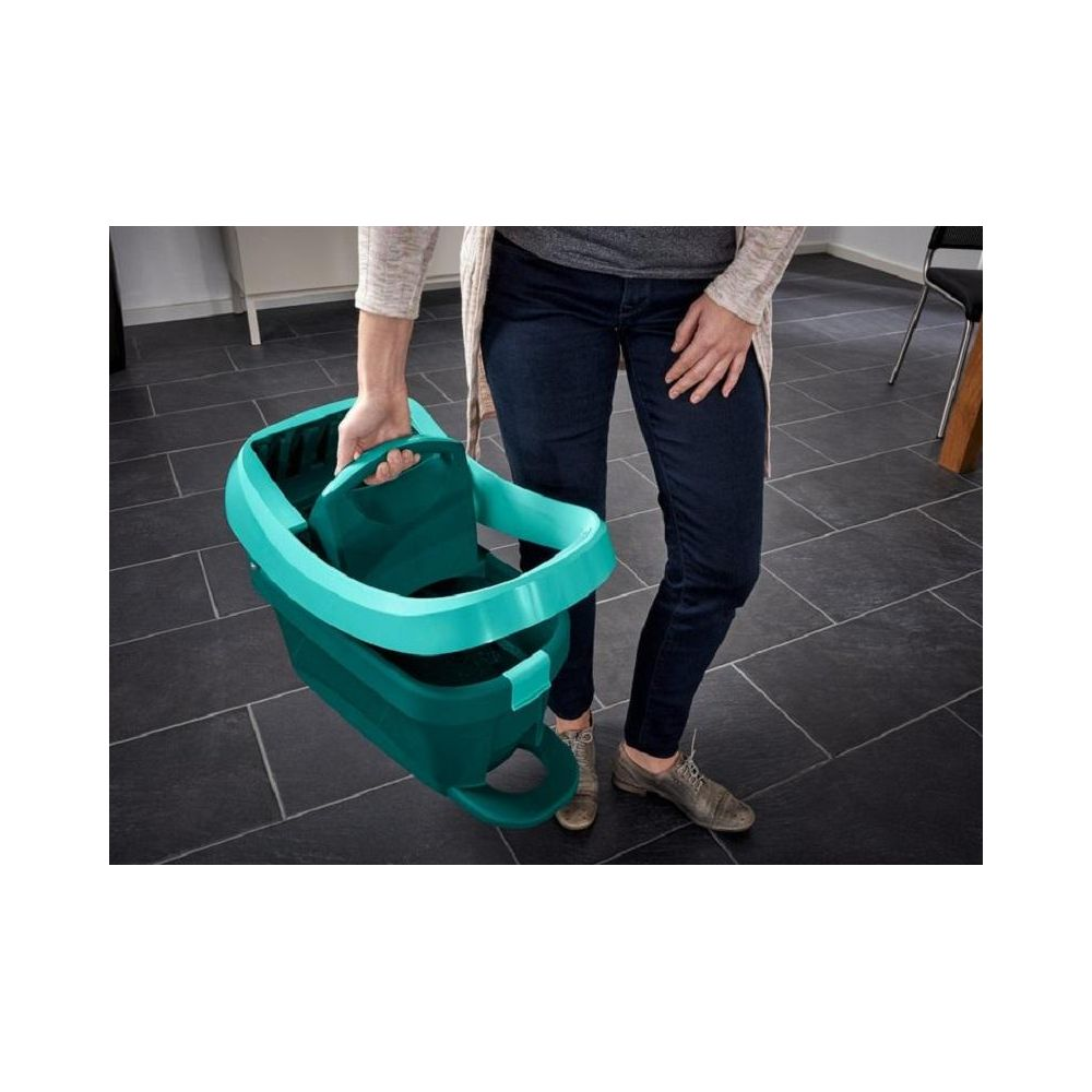 Osoba trzymająca turkusowe wiadro z uchwytami na ciemnej podłodze.