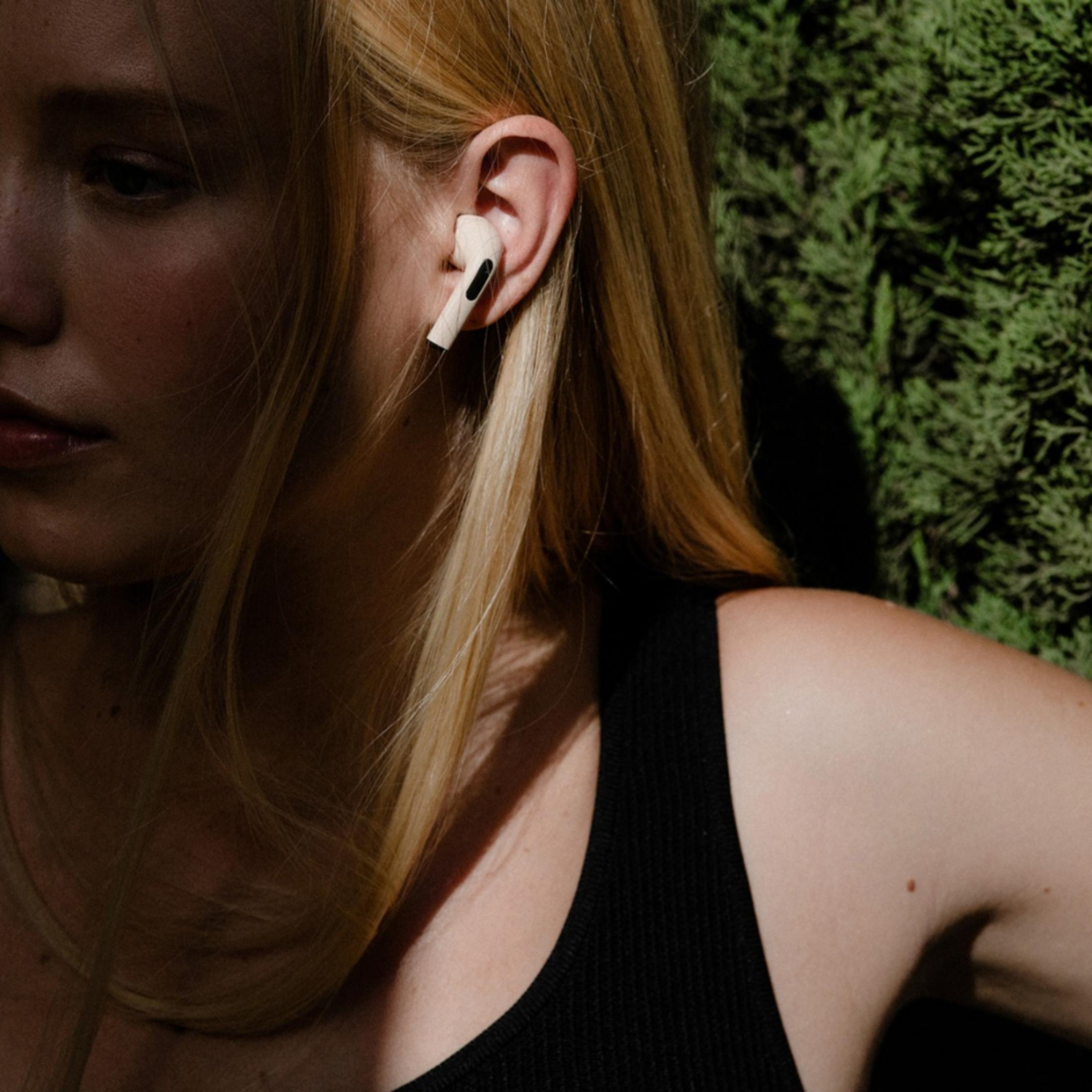 Kobieta z blond włosami nosi białą słuchawkę w uchu. Ma na sobie czarną bluzkę.