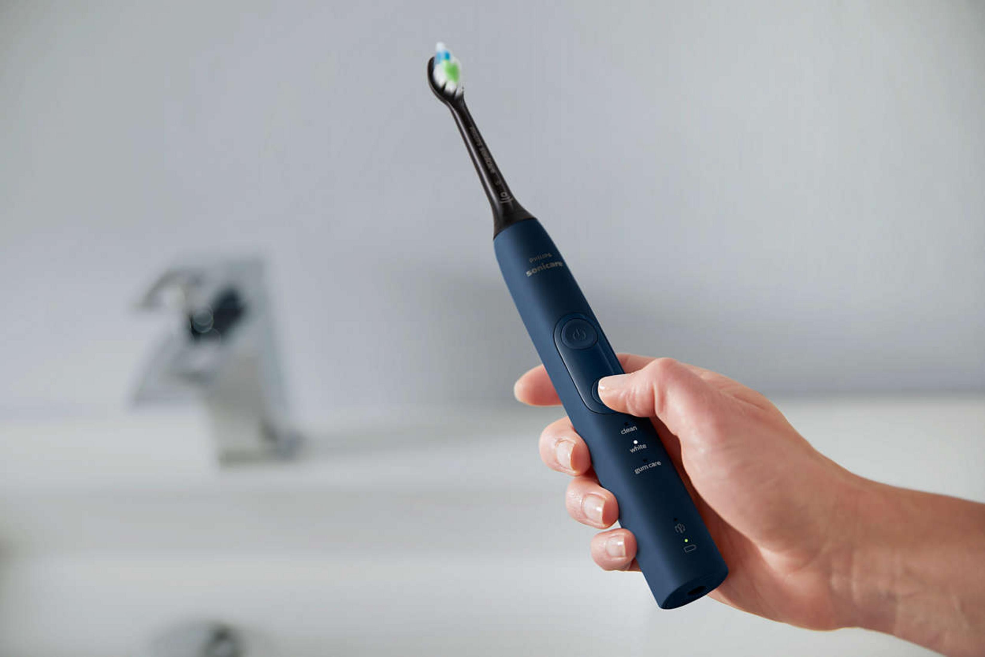 Spazzolino elettrico blu con setole blu, verdi e bianche tenuto.