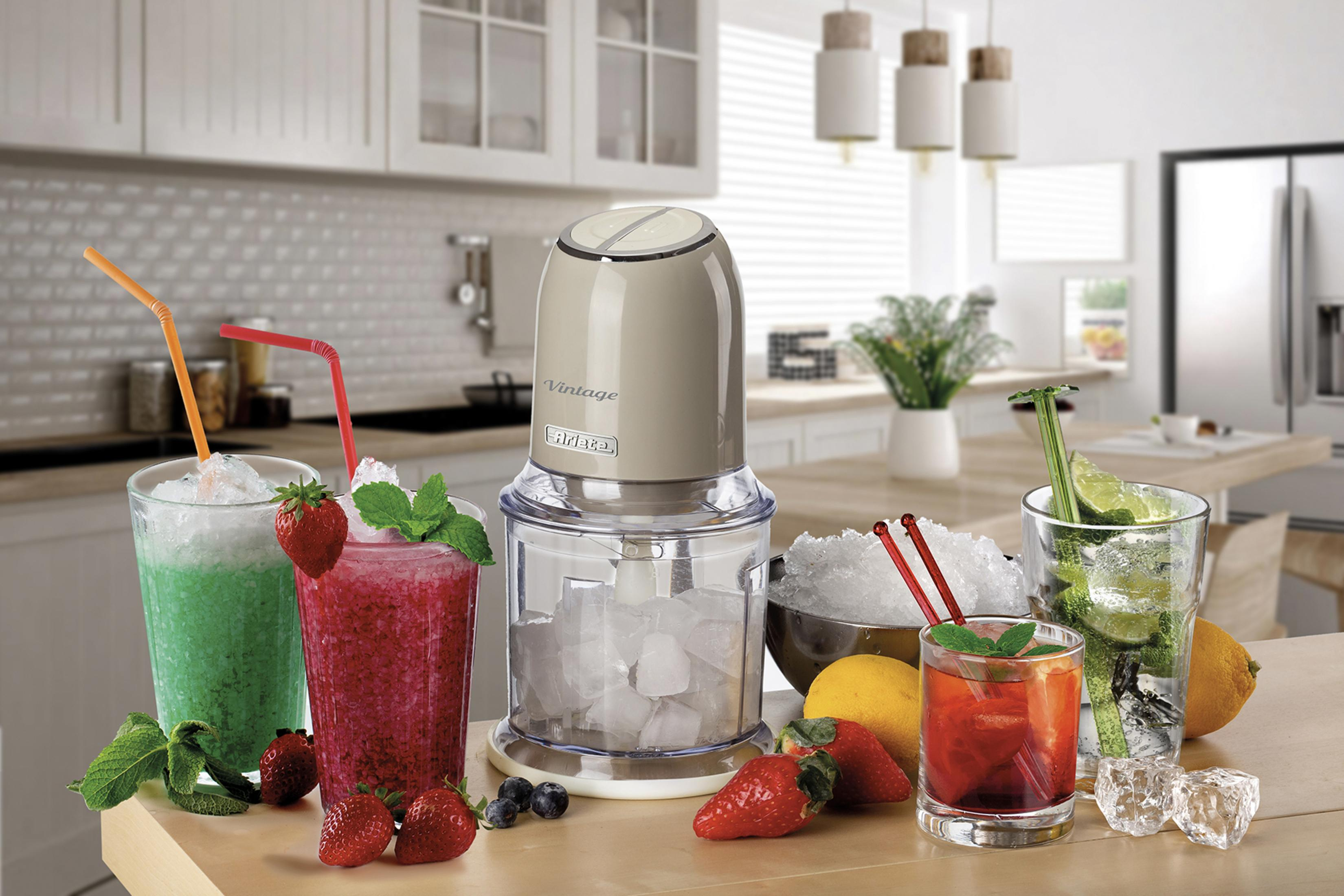 Bir mutfakta renkli içecekler, buz ve meyvelerin yanında bir blender duruyor.