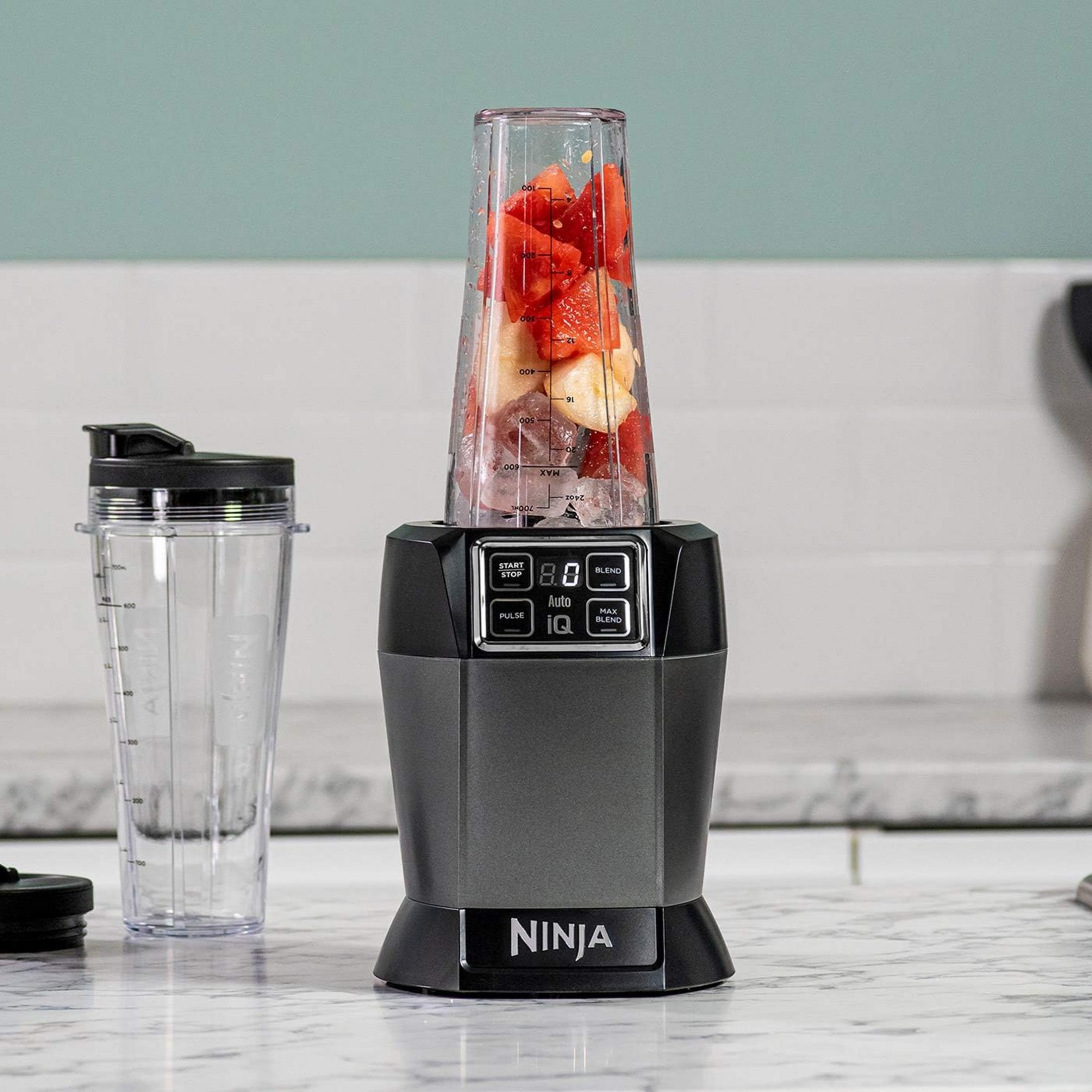 Una licuadora Ninja con fruta y hielo en un vaso, junto a un vaso vacío.