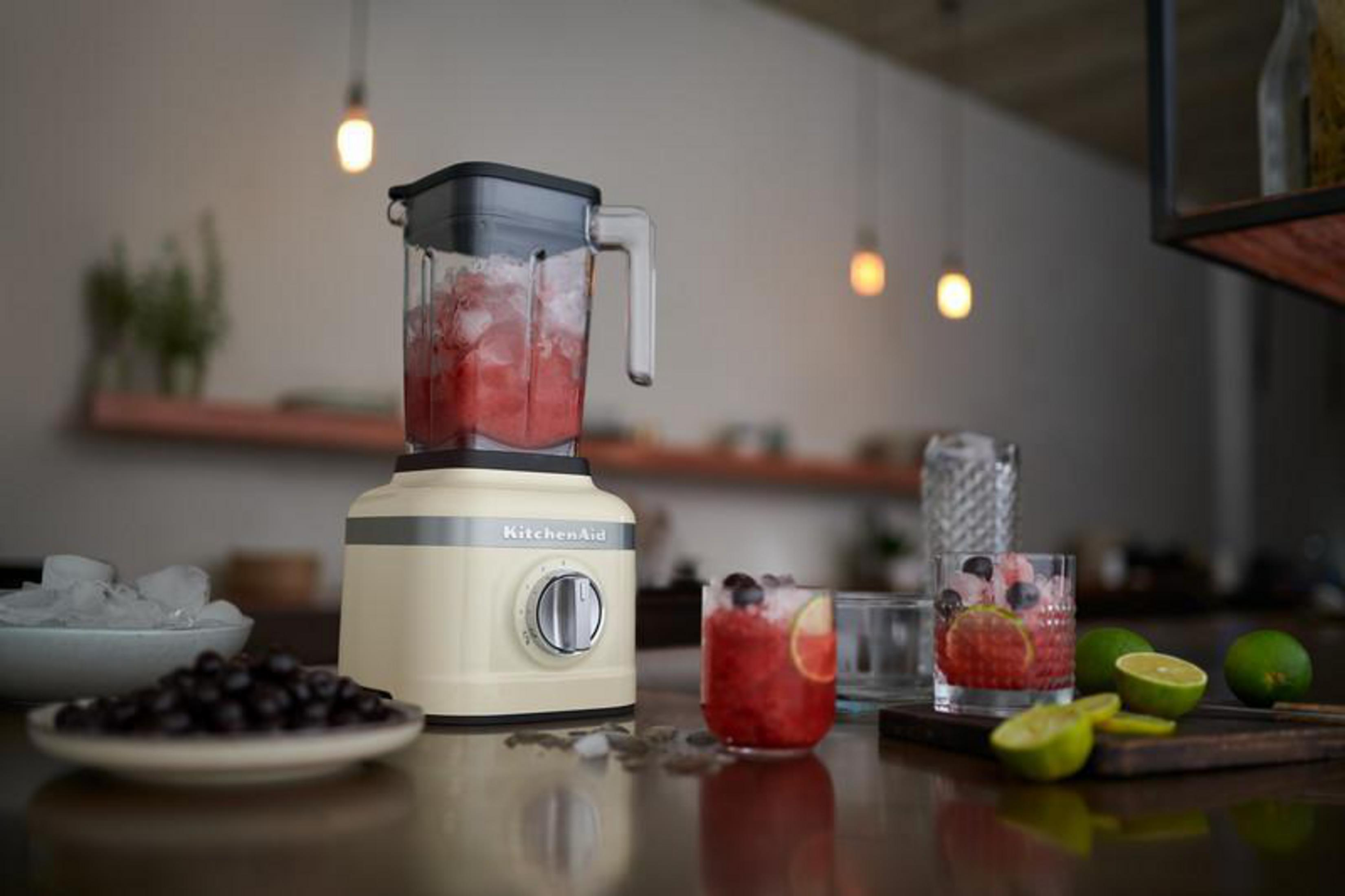 A cream-colored blender with ice and fruit mixture, next to two glasses of drinks.