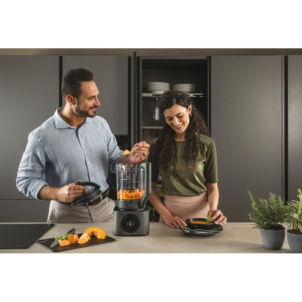 Uomo e donna preparano cibo. Uomo aggiunge zucca a frullatore, donna guarnisce zuppa.