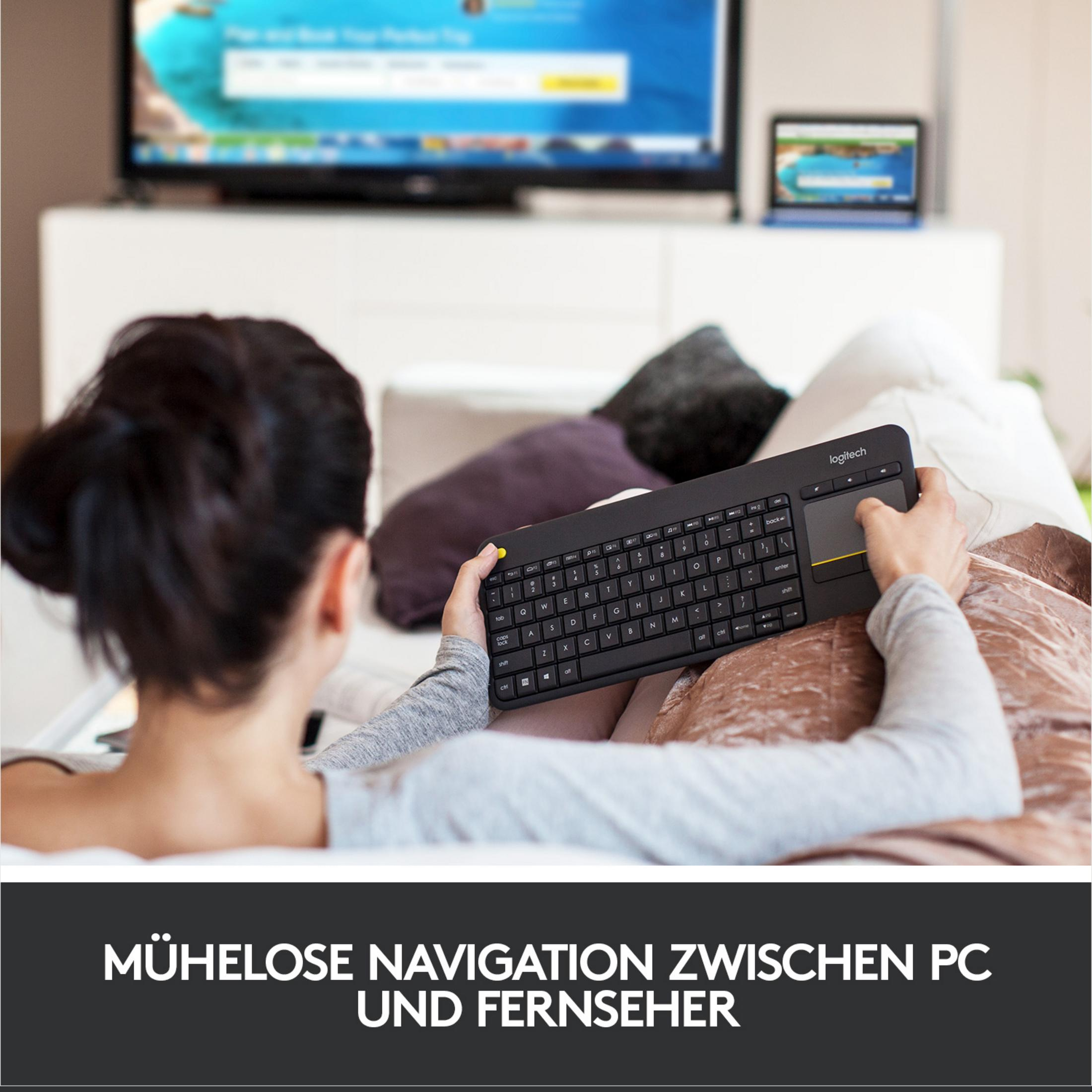 Person hält Tastatur mit Touchpad, schaut auf TV und Laptop. Entspannt.
