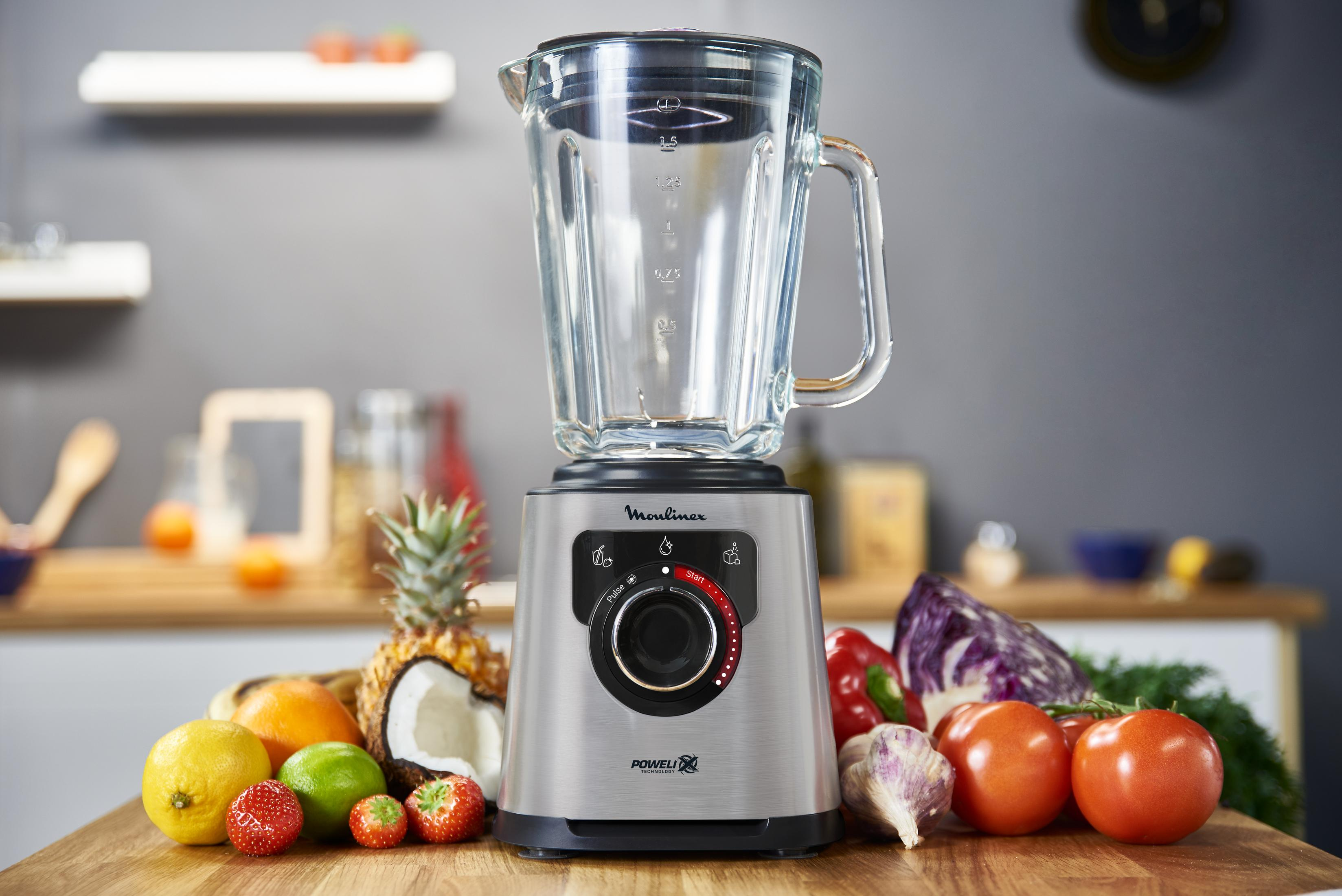 Ein Mixer steht auf einem Holztisch mit Obst und Gemüse.