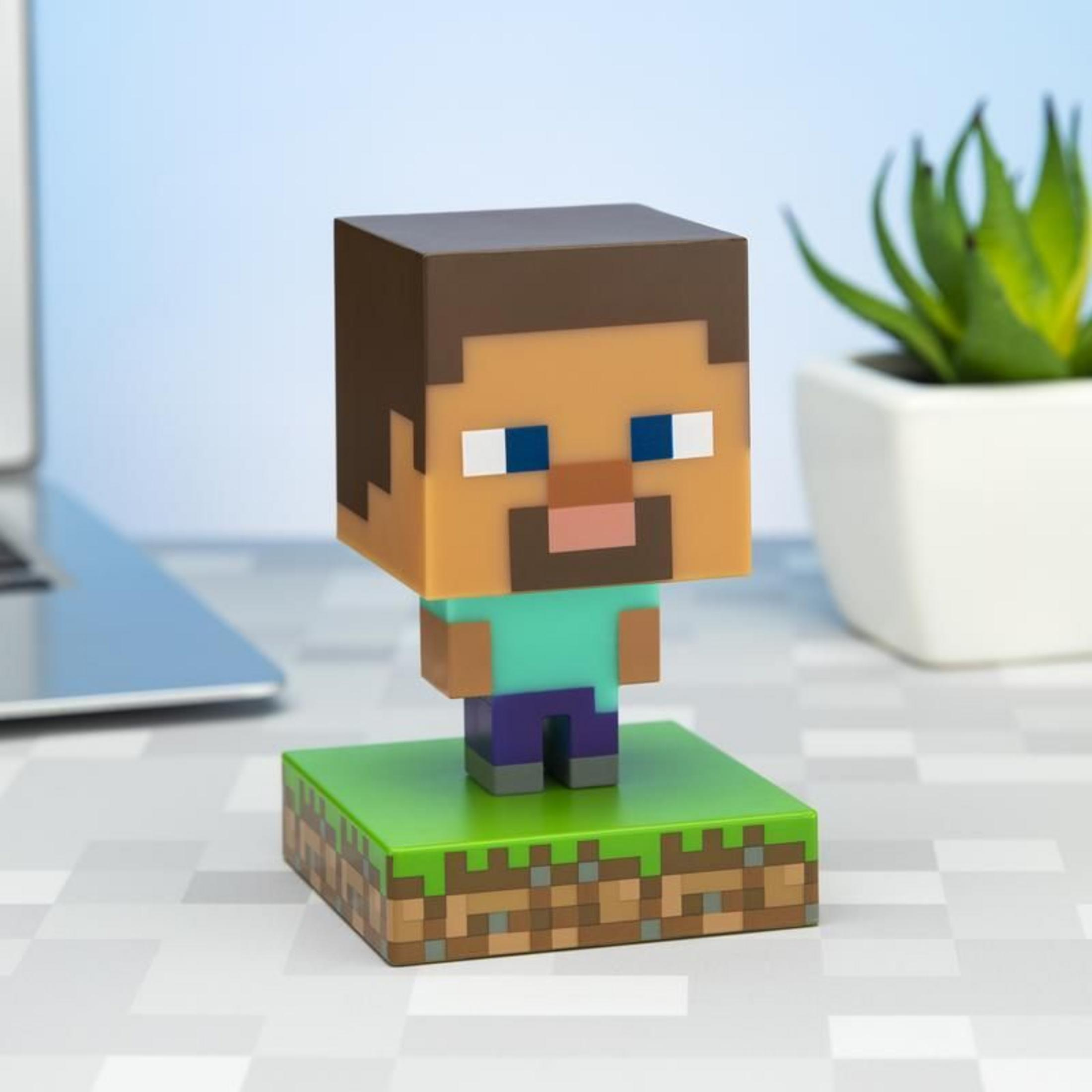 Figura de Minecraft Steve sobre una base de bloque de hierba. Portátil y planta al fondo.