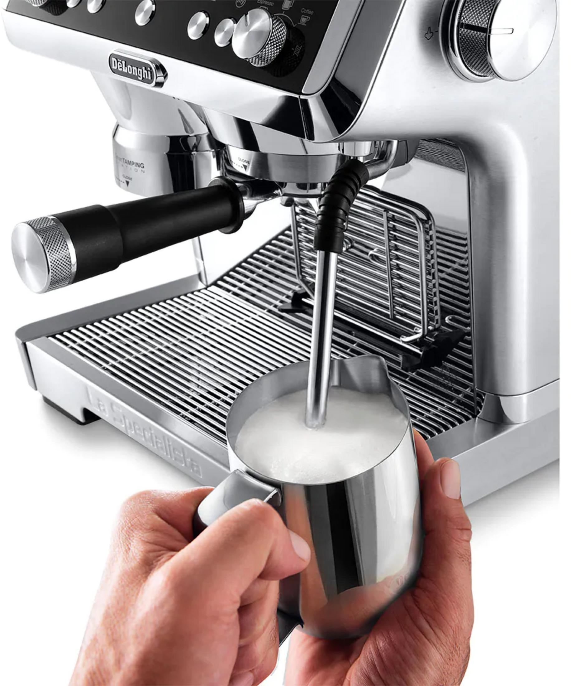 Eine Hand hält einen Milchbehälter unter einer Espressomaschine, die Milch aufschäumt.
