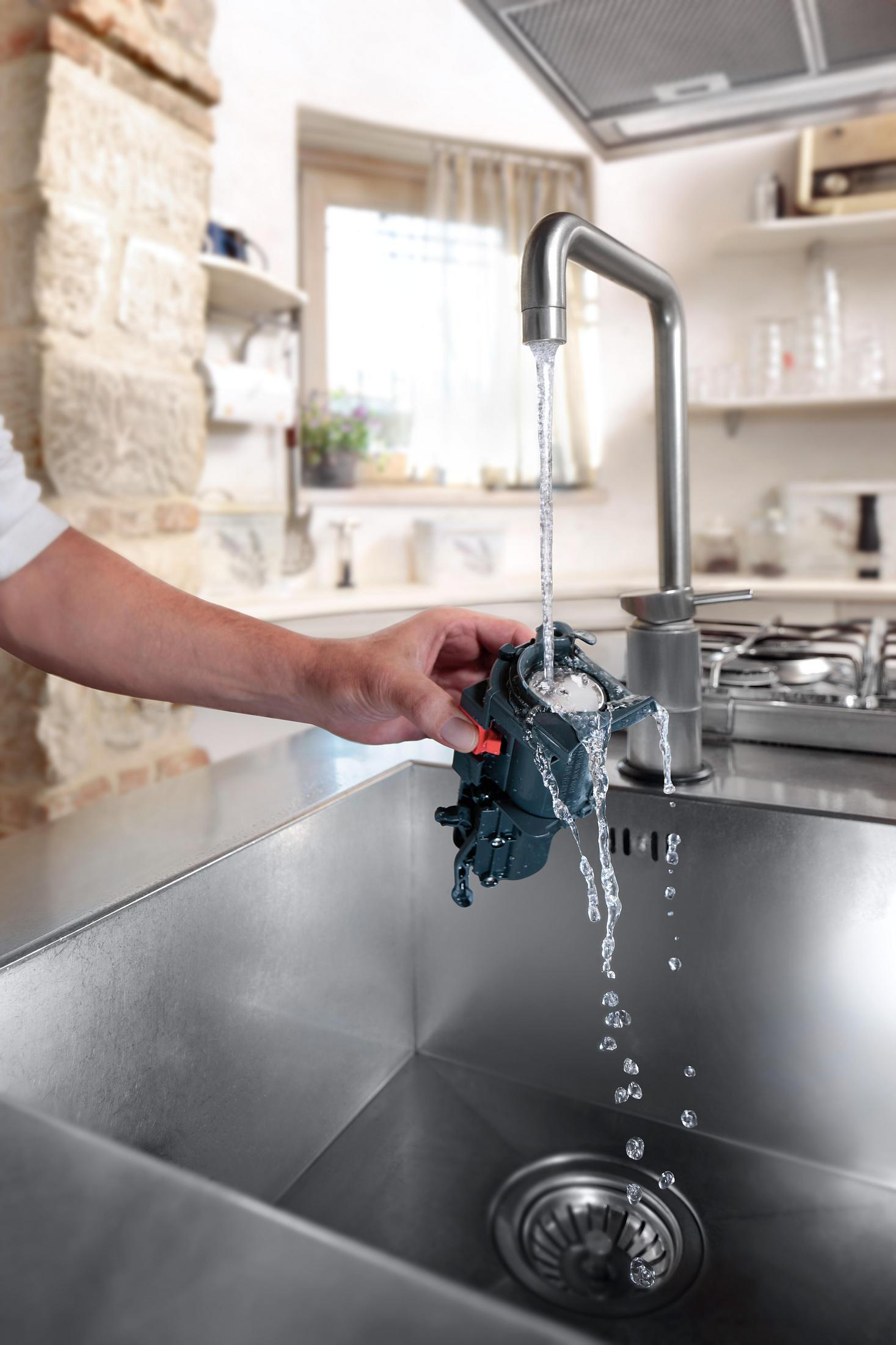Eine Hand hält ein dunkles Gerät unter fließendes Wasser in einer Spüle.