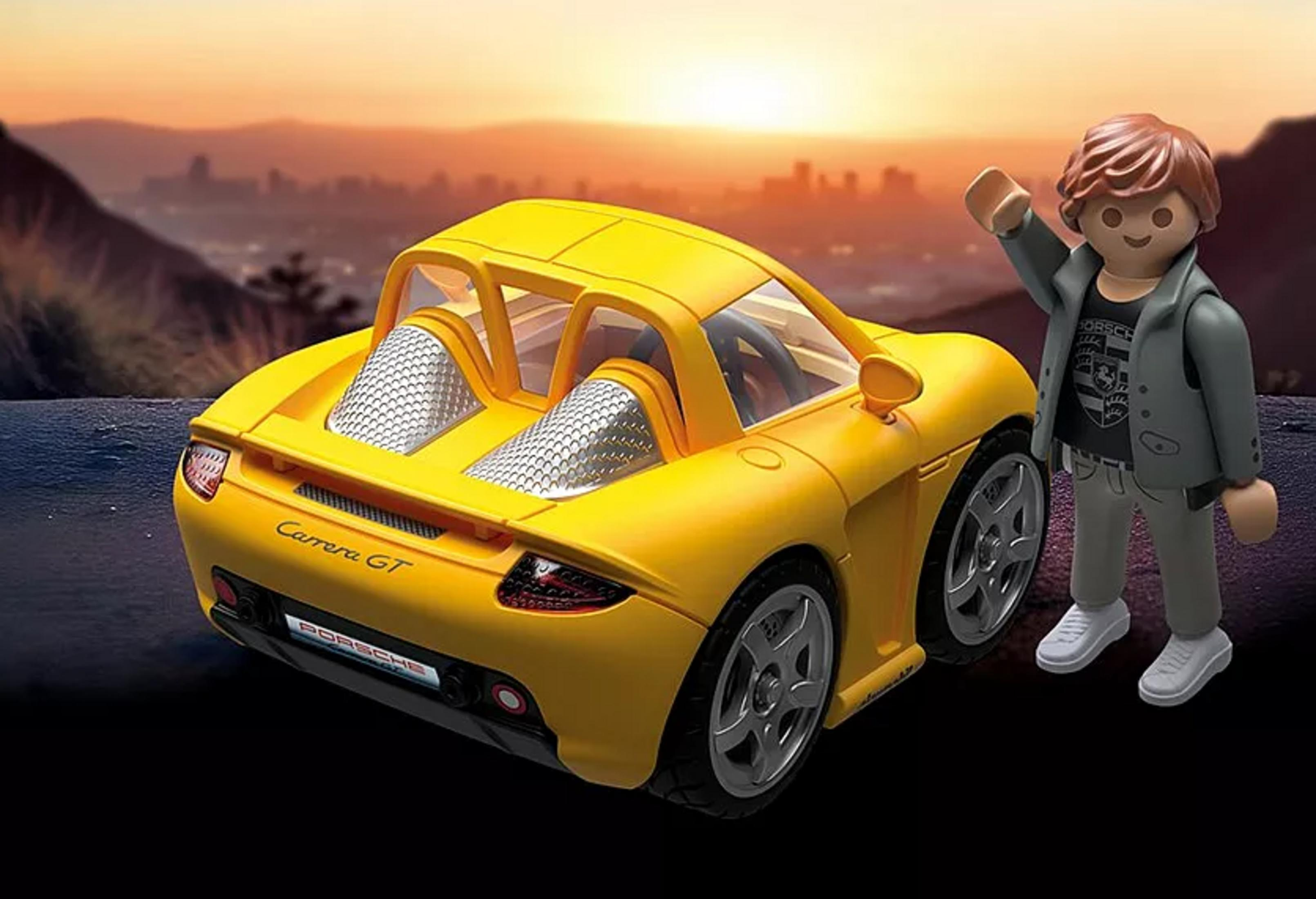 Un Porsche Carrera GT amarillo con una figura de juguete al lado al atardecer.
