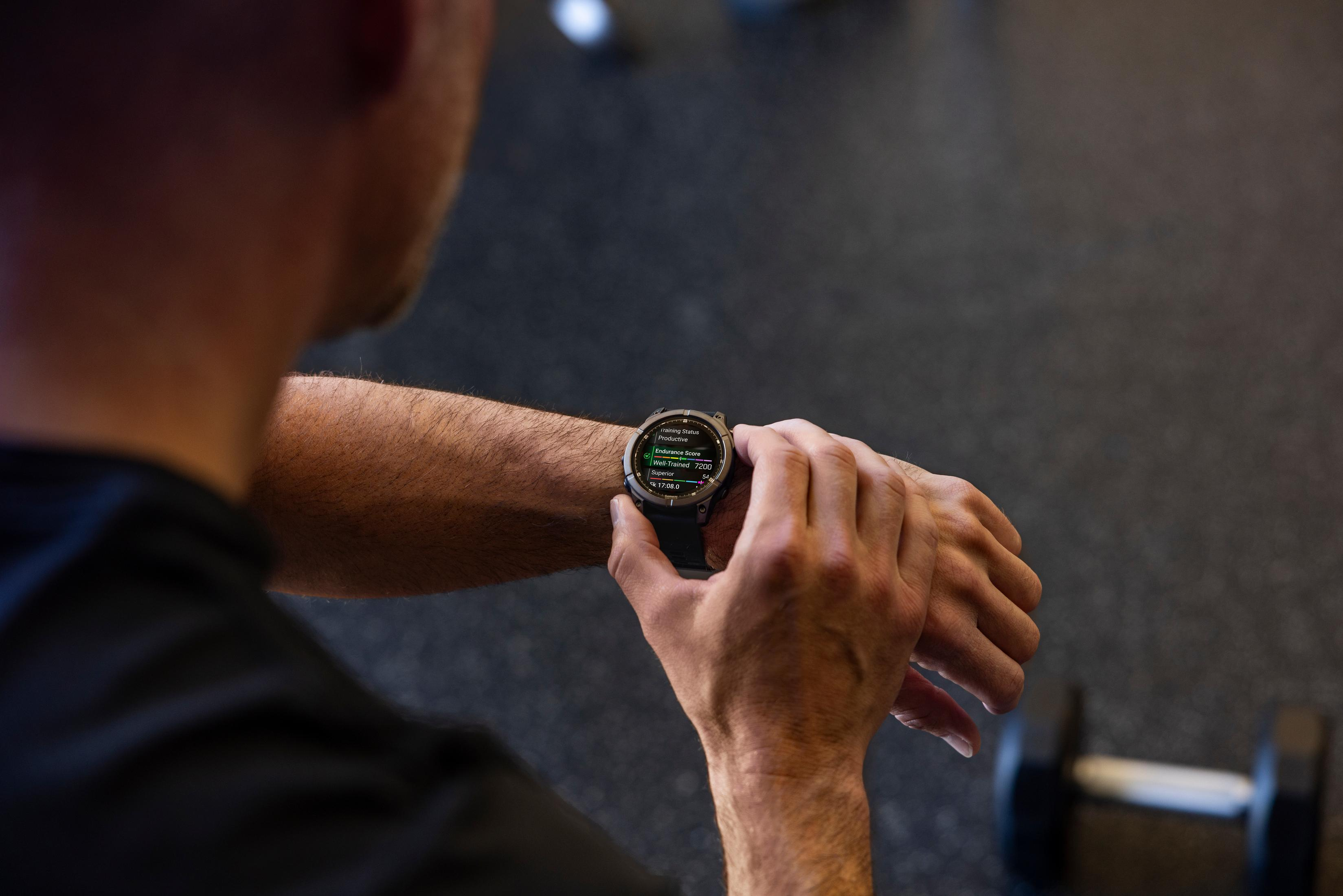 Mężczyzna sprawdza zegarek sportowy pokazujący statystyki treningu. Hantle w tle.