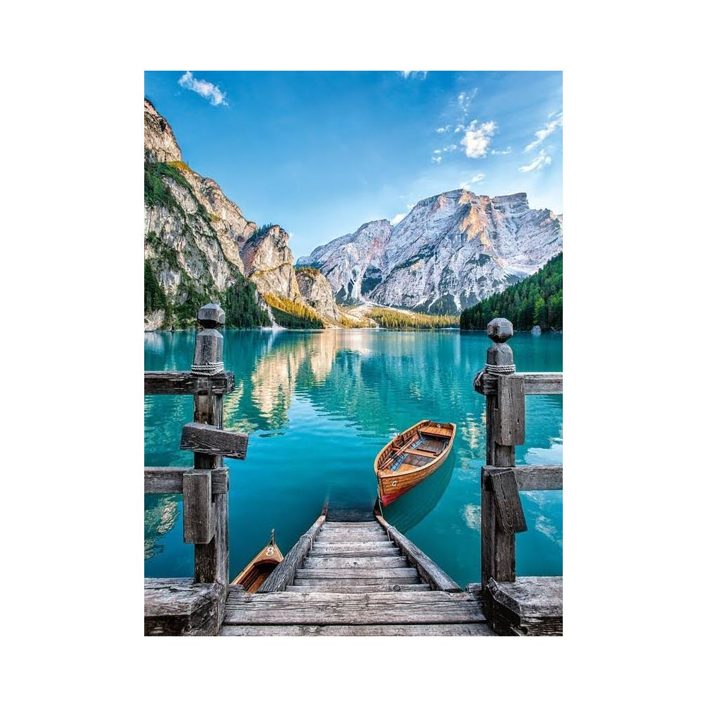 Molo in legno con barche su un lago turchese con montagne sullo sfondo.