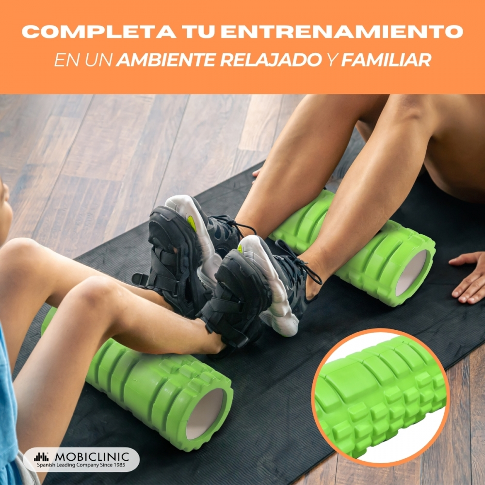 Dos personas usan rodillos de espuma verdes en una esterilla, masajeando sus piernas.