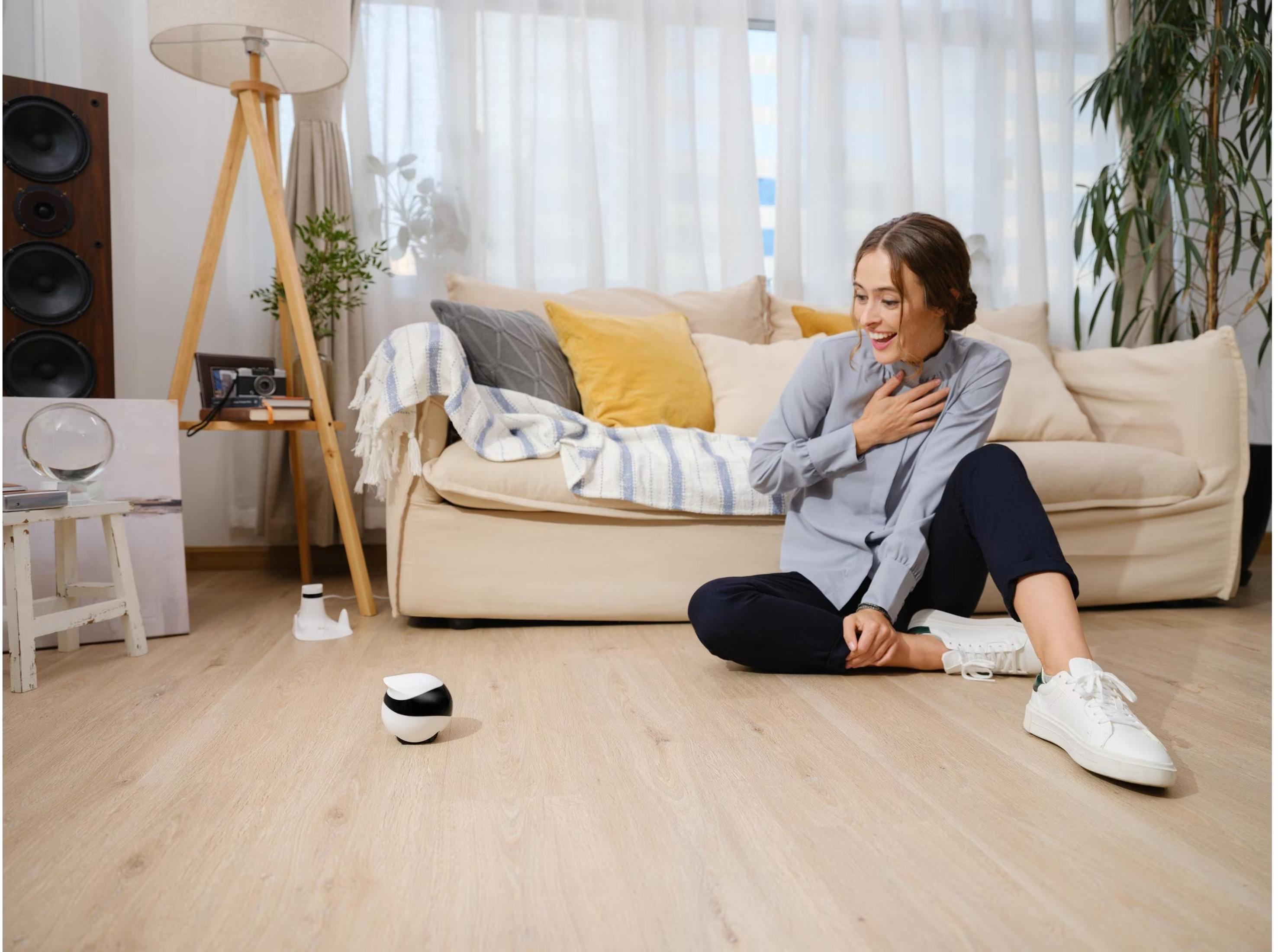 Eine Frau sitzt auf dem Boden vor einem Sofa, neben einem kleinen Roboter.
