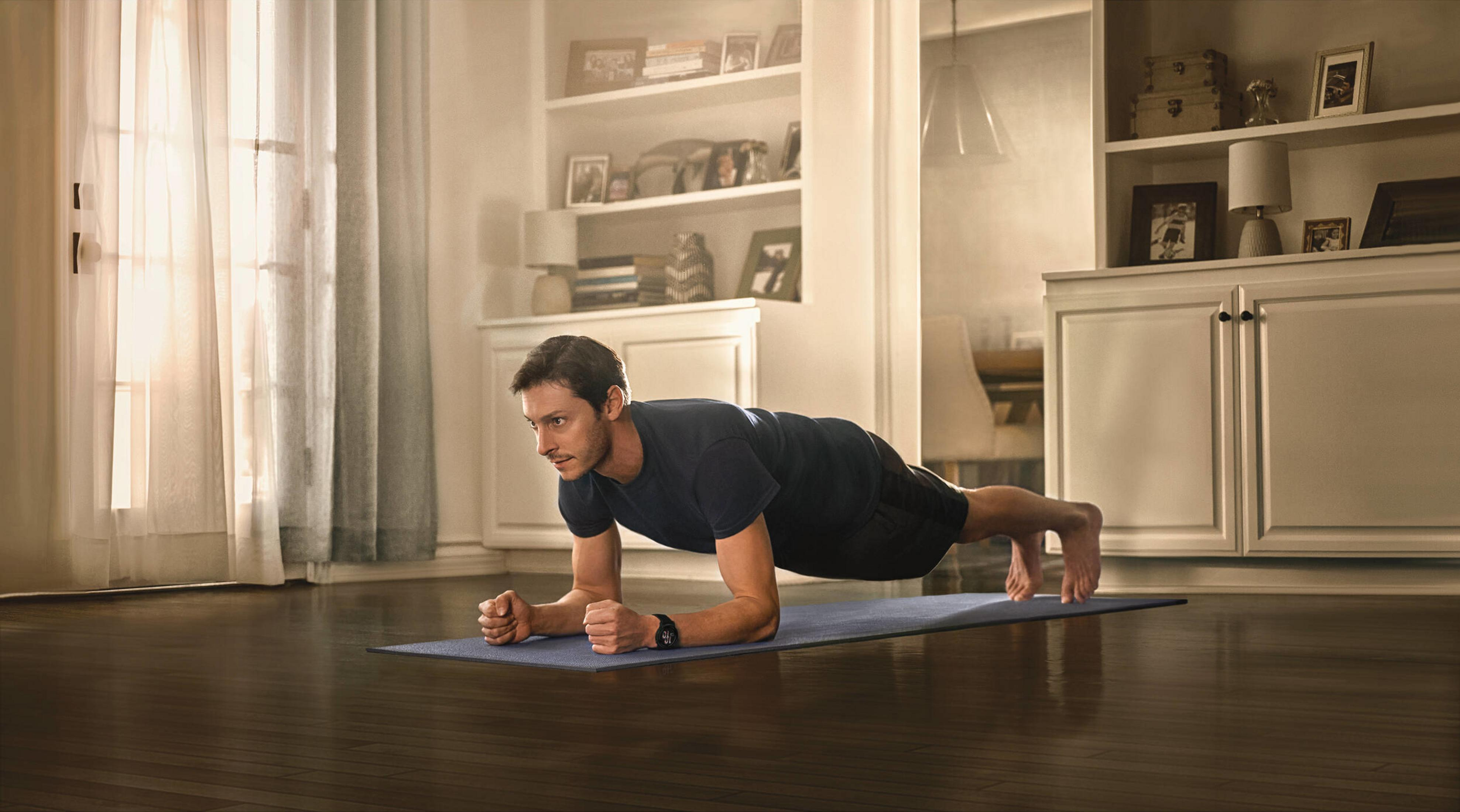 Mann in Unterarmstützposition auf einer Matte in einem Wohnzimmer.