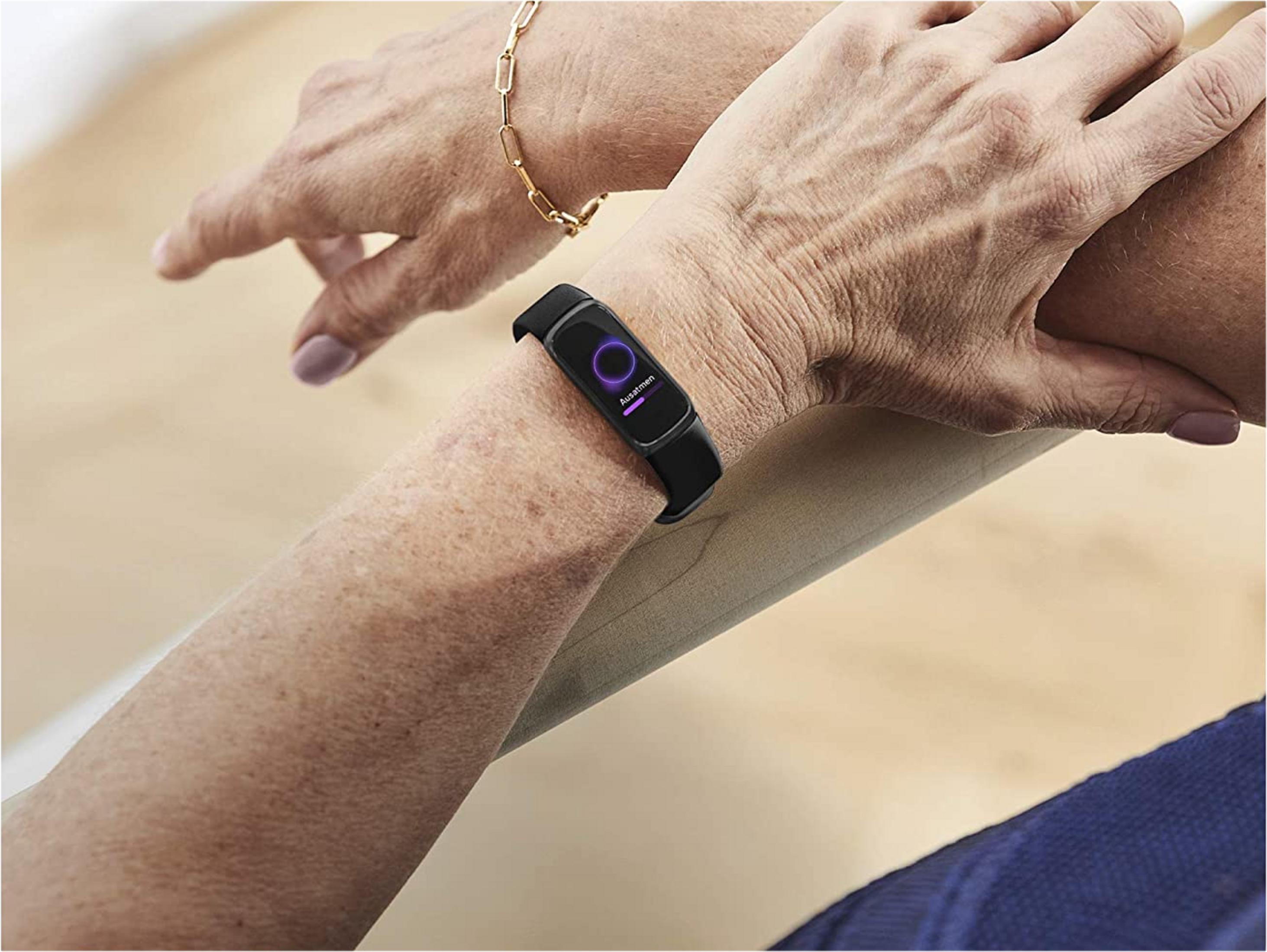 Eine Person trägt einen schwarzen Fitness-Tracker am Handgelenk, der 'Ausatmen' anzeigt.