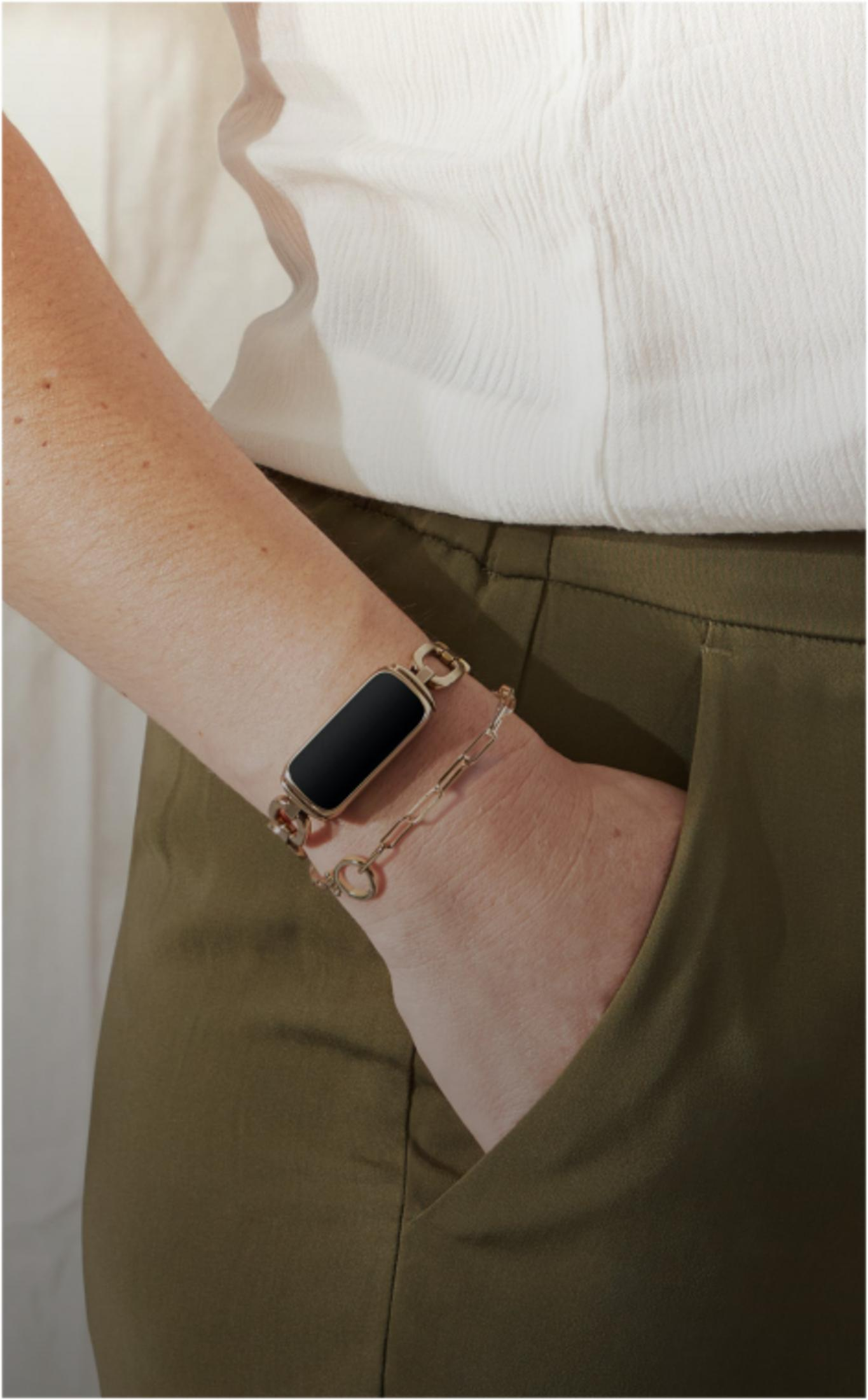 Arm mit schwarzem Fitness-Tracker und Goldarmband trägt khaki Hose.