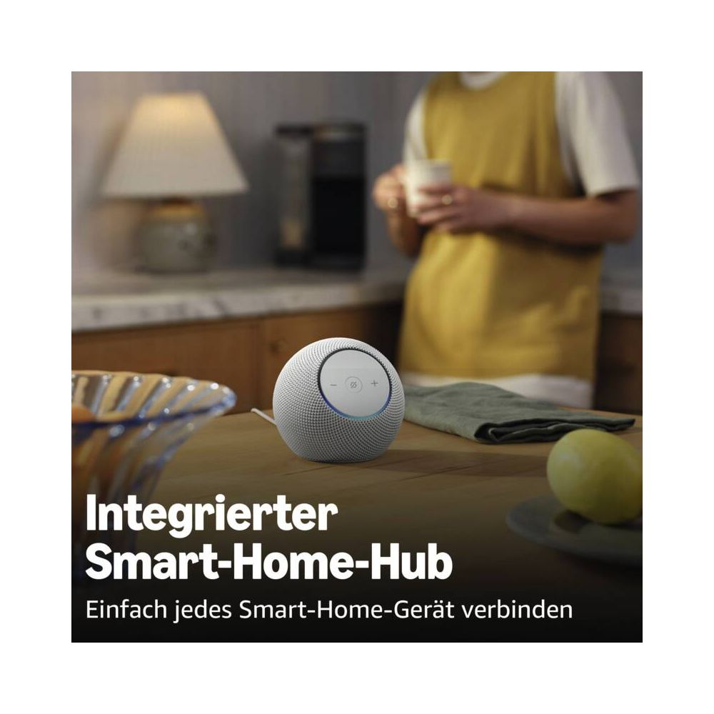 Ein weißer Smart Speaker steht auf einem Holztisch. Im Hintergrund eine Person.