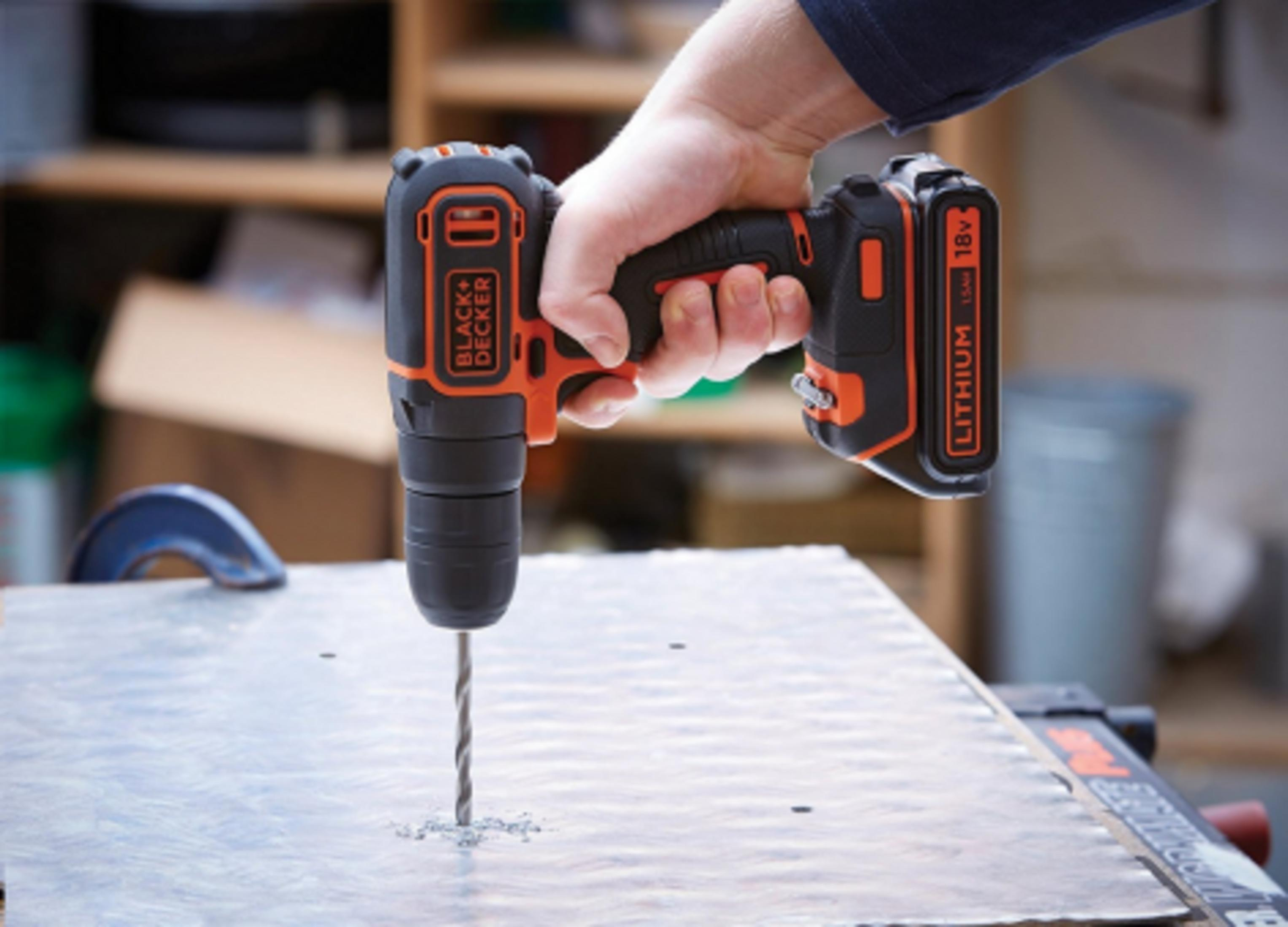 Ręka trzyma czarno-pomarańczową wiertarkę akumulatorową wiercącą w metal.