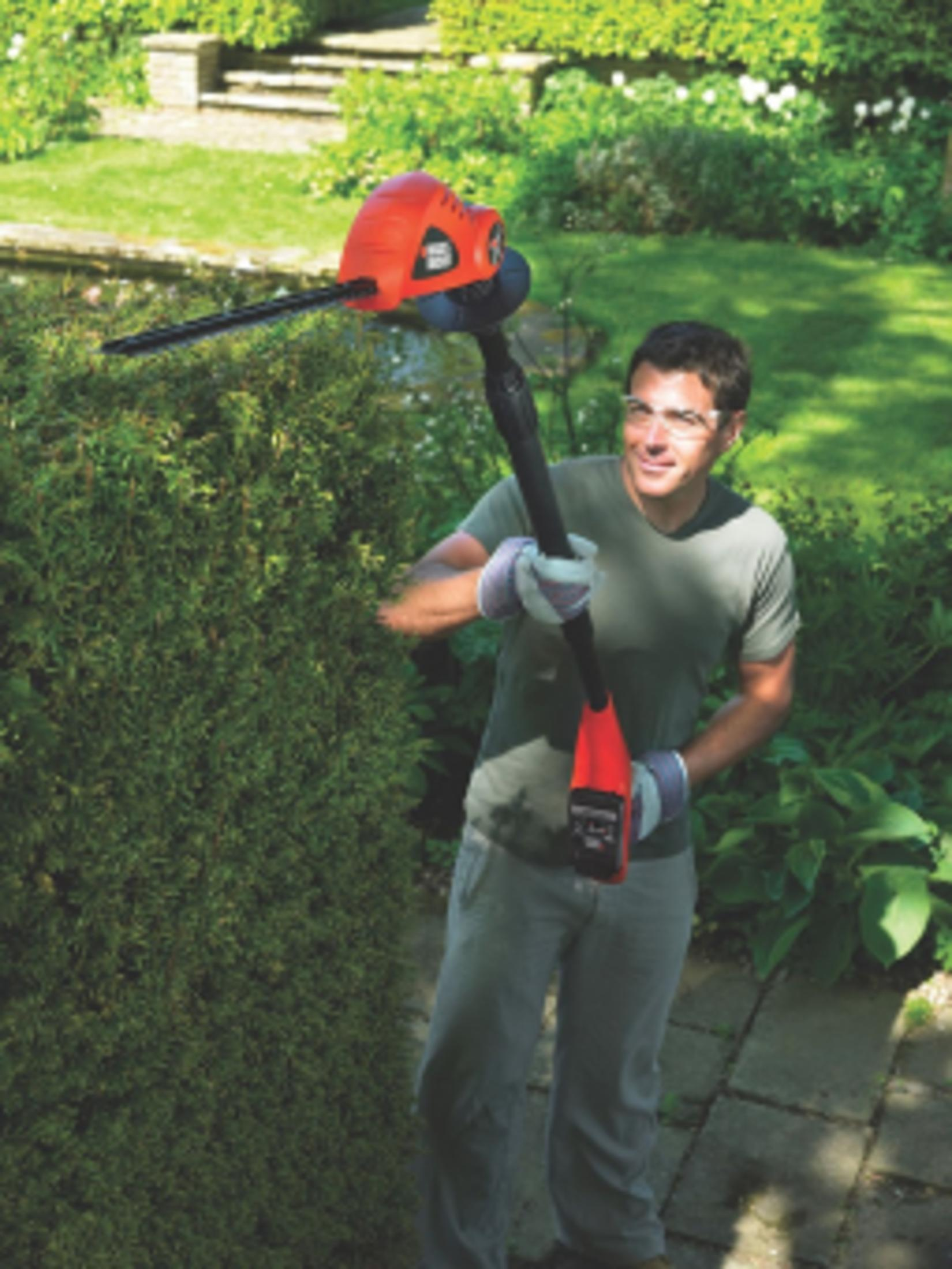 Mężczyzna przycina żywopłot nożycami elektrycznymi na zewnątrz.