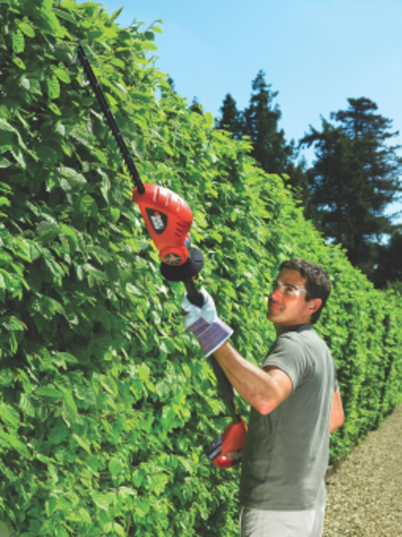 Mężczyzna przycina żywopłot nożycami elektrycznymi na zewnątrz.