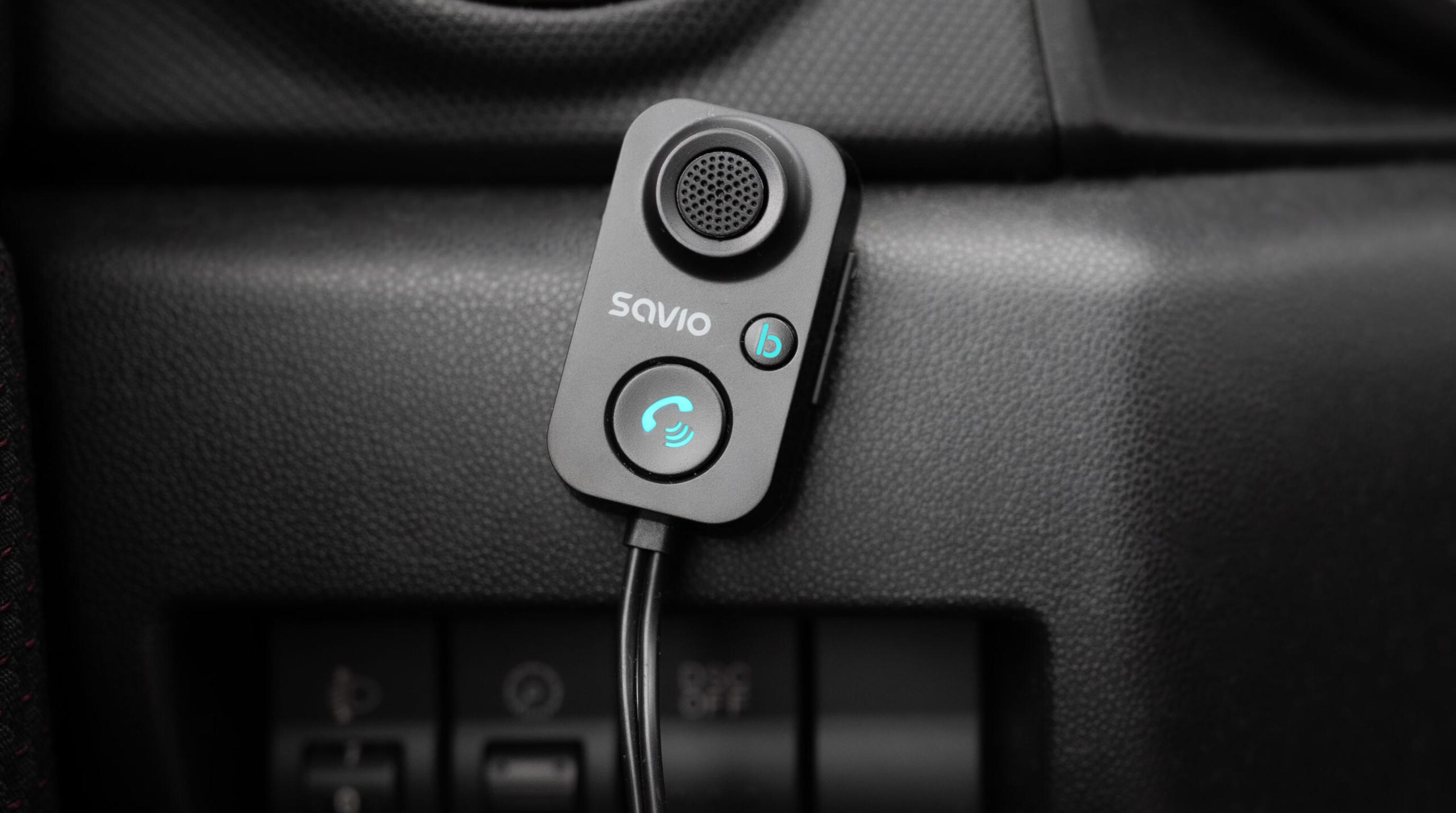 Szary odbiornik Bluetooth z mikrofonem i niebieskimi ikonami w samochodzie.