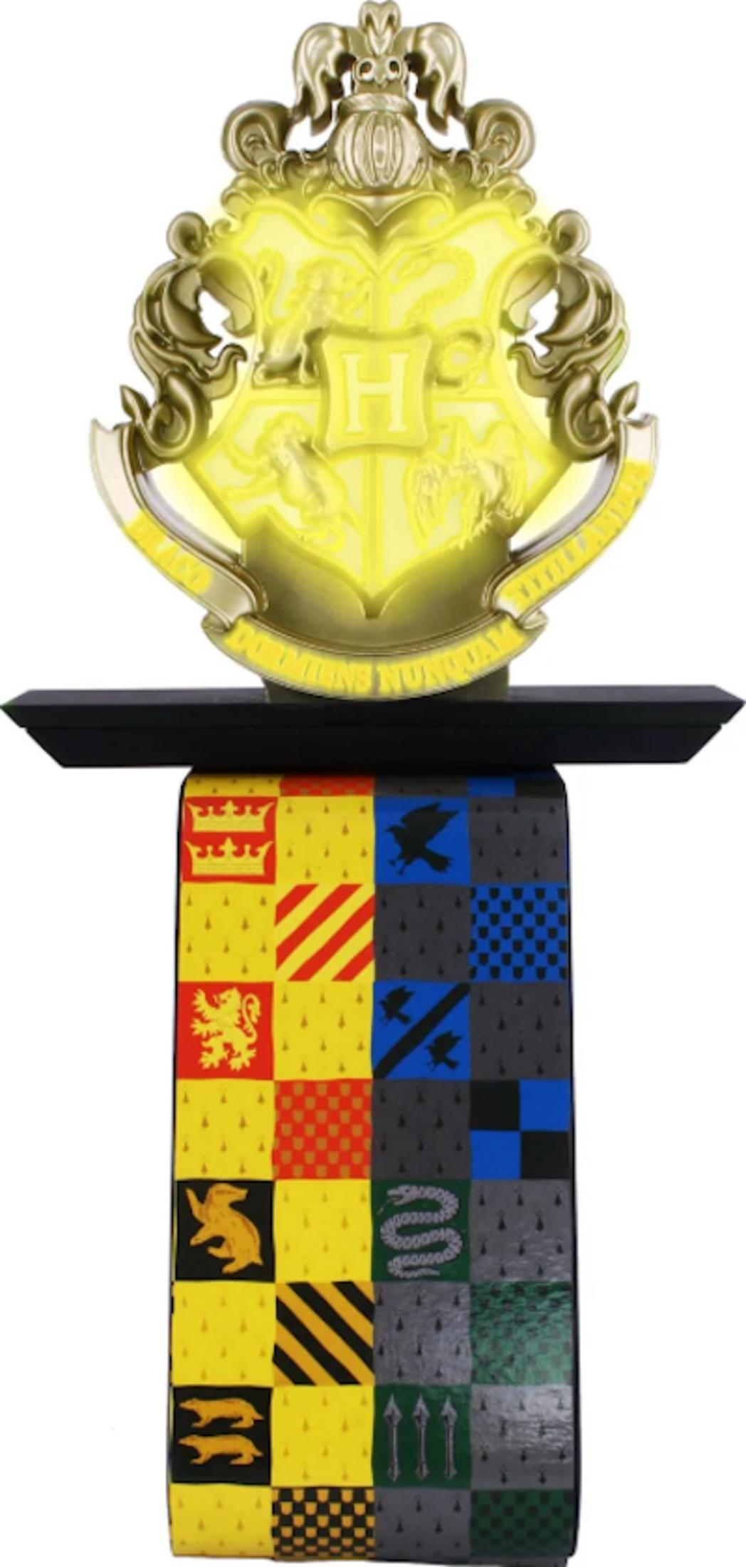 Uno stemma di Hogwarts luminoso sopra un tessuto colorato con stemmi.