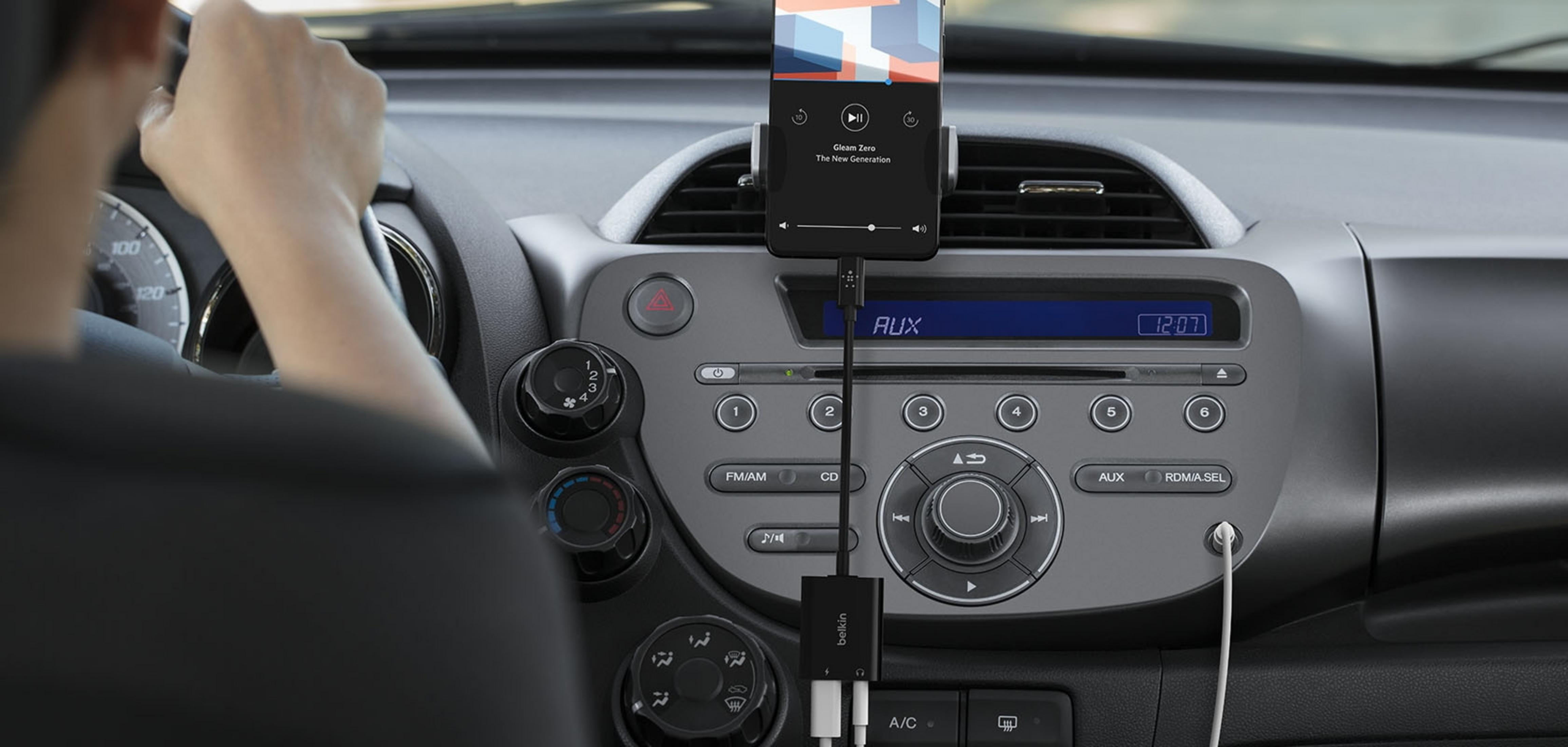 Una persona guida un'auto, telefono collegato all'ingresso aux.