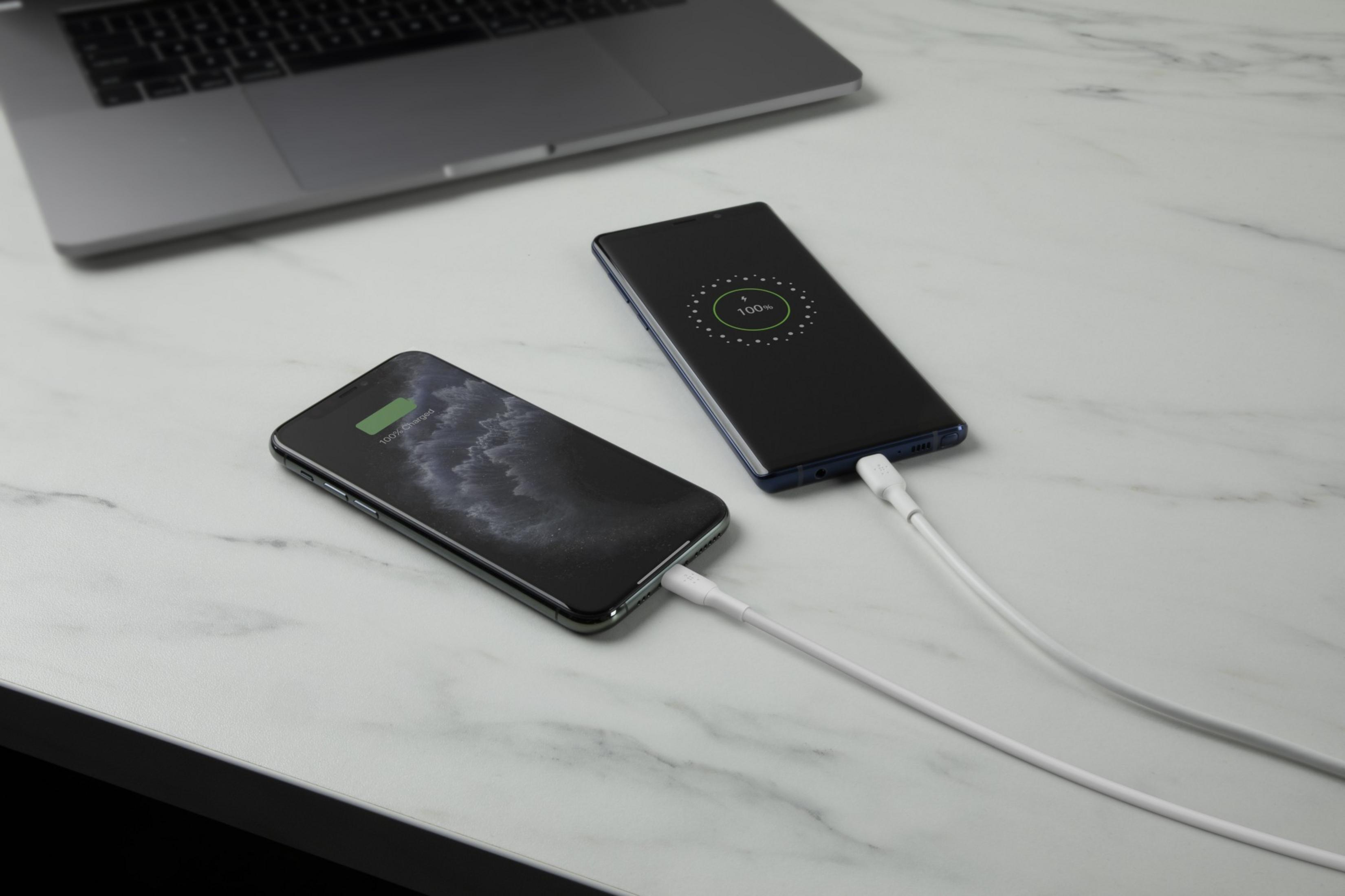 Due smartphone e un laptop in carica su una superficie di marmo.