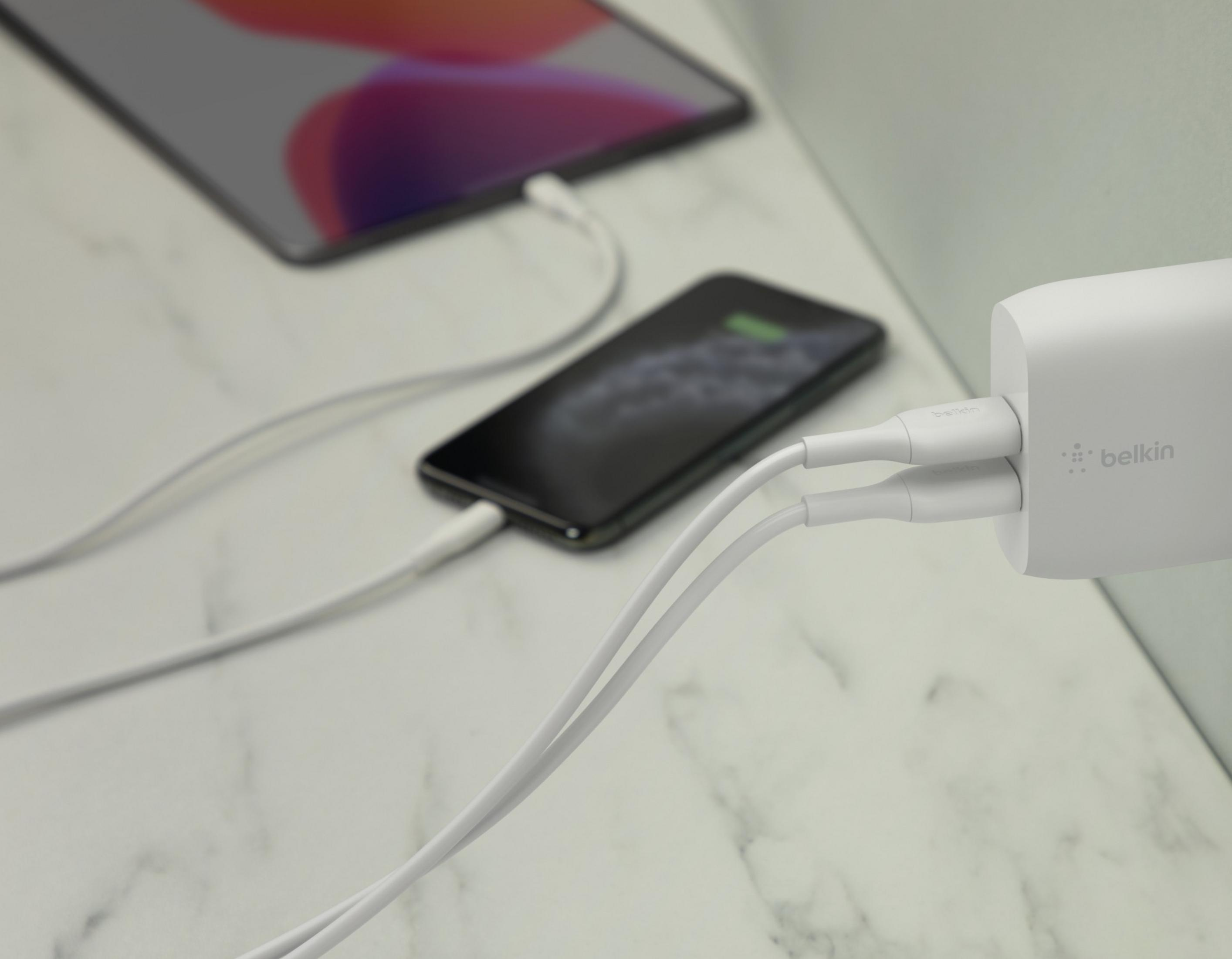 Un caricabatterie Belkin bianco alimenta un iPhone e un tablet con cavi bianchi.