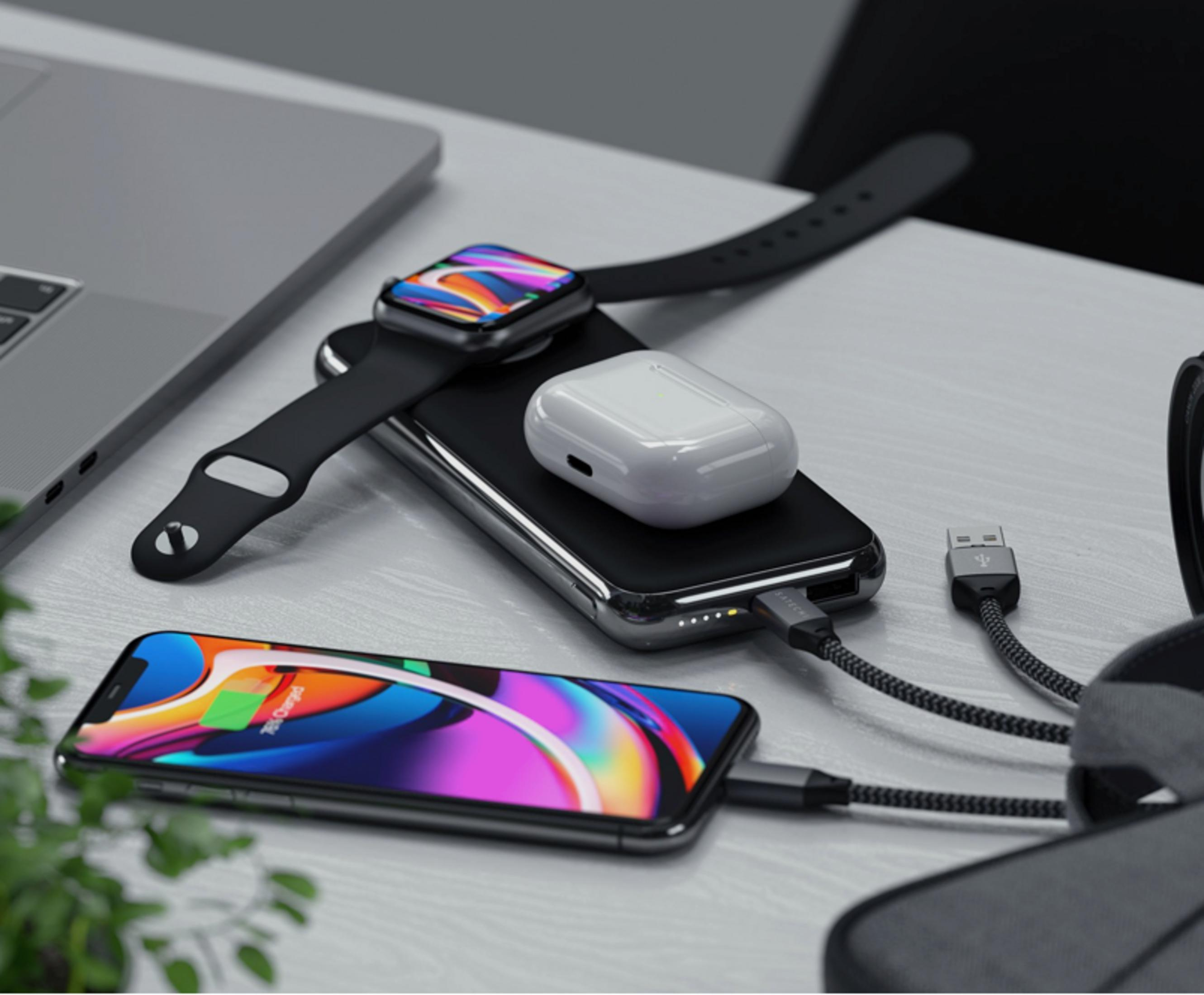 Un laptop, smartphone, smartwatch e auricolari in carica su un tavolo.