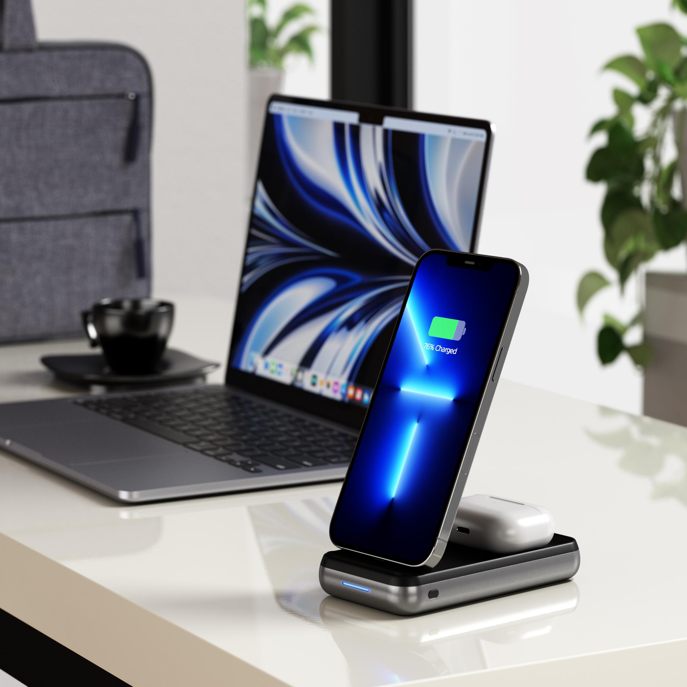 Ein Smartphone wird auf einer Ladestation aufgeladen, daneben ein Laptop, Kopfhörer und eine Tasche.