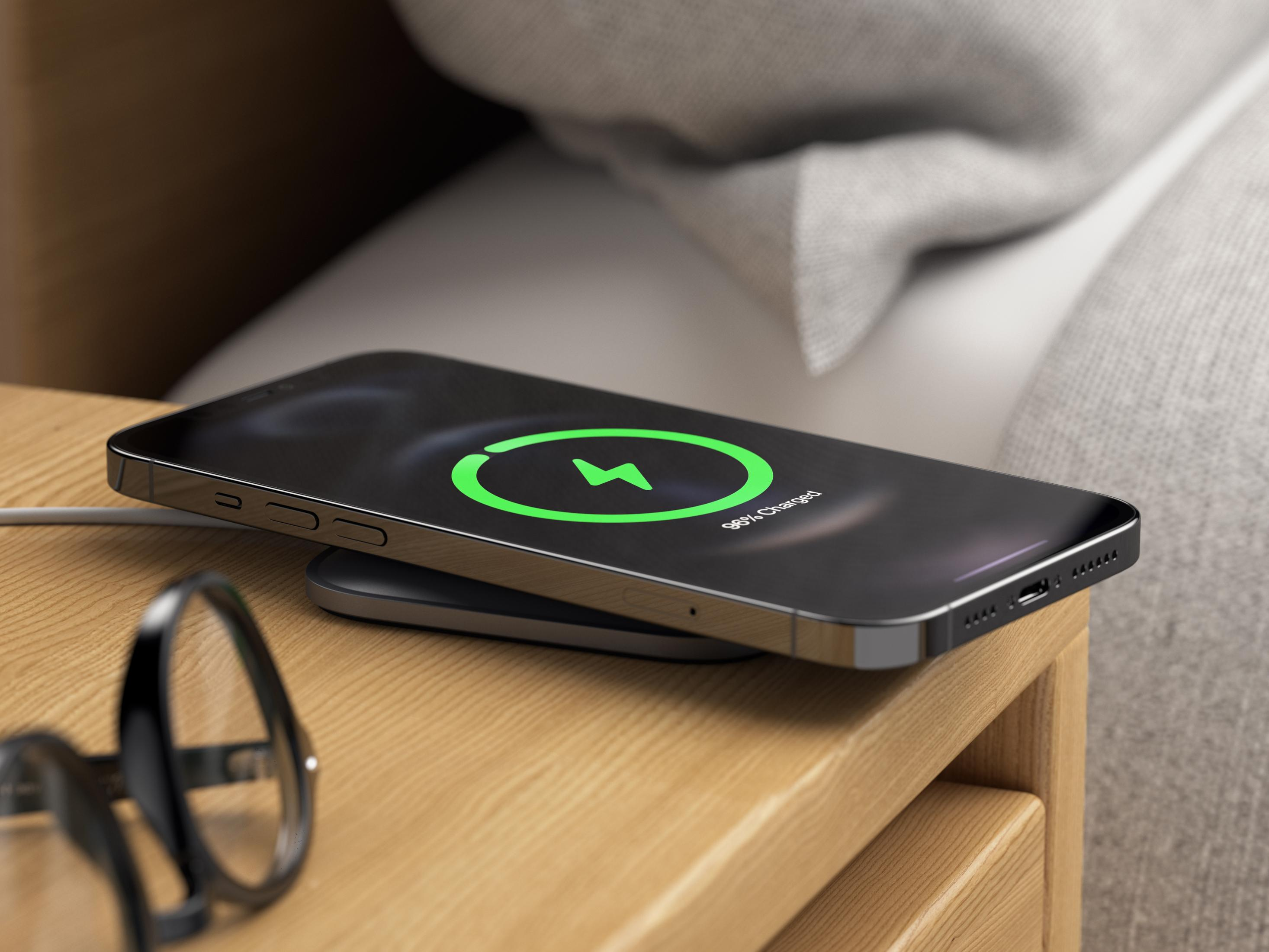Smartphone lädt auf einem Nachttisch mit Brille.