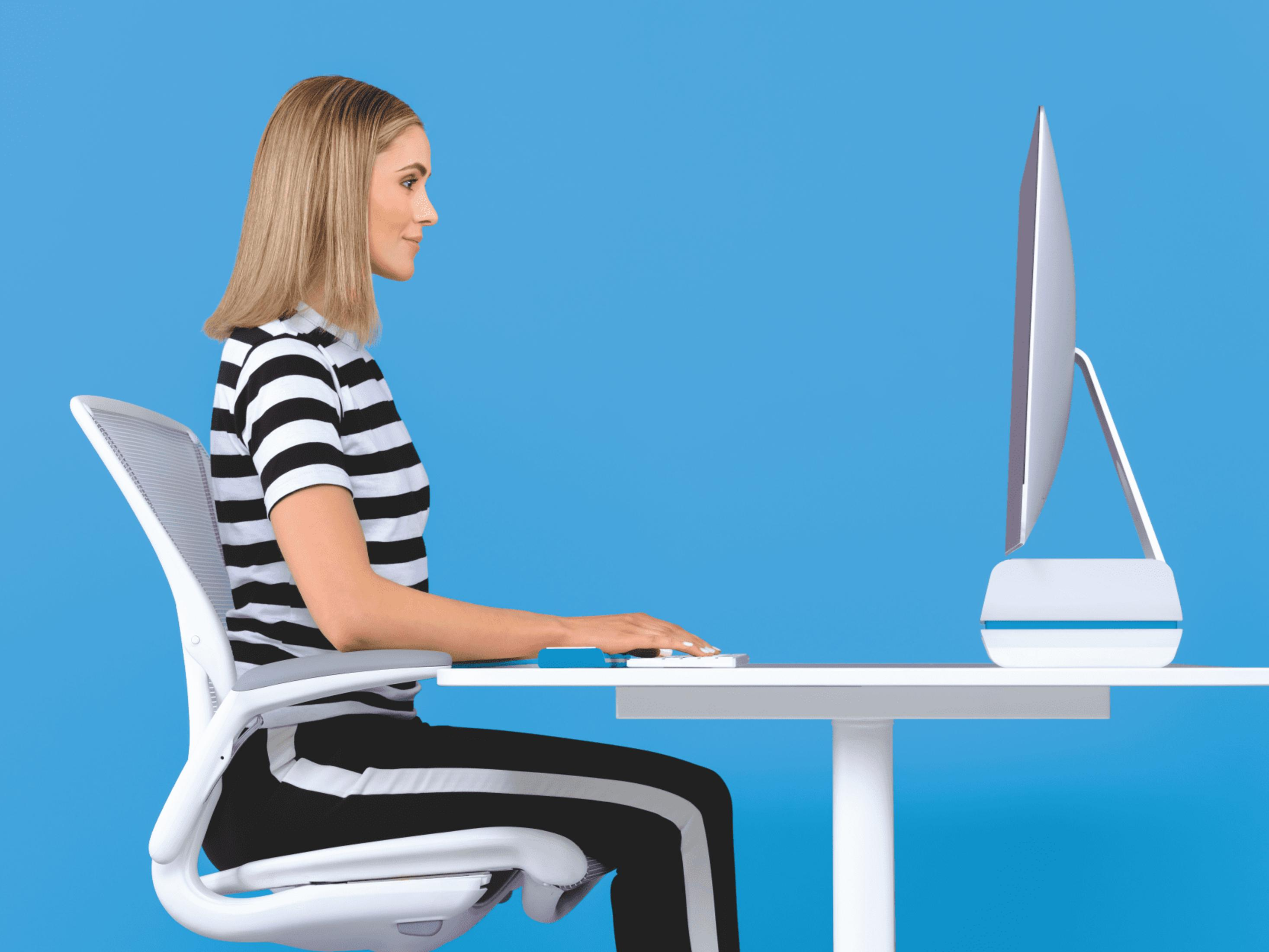 Kobieta siedzi przy biurku, pisząc na klawiaturze przed monitorem komputera.