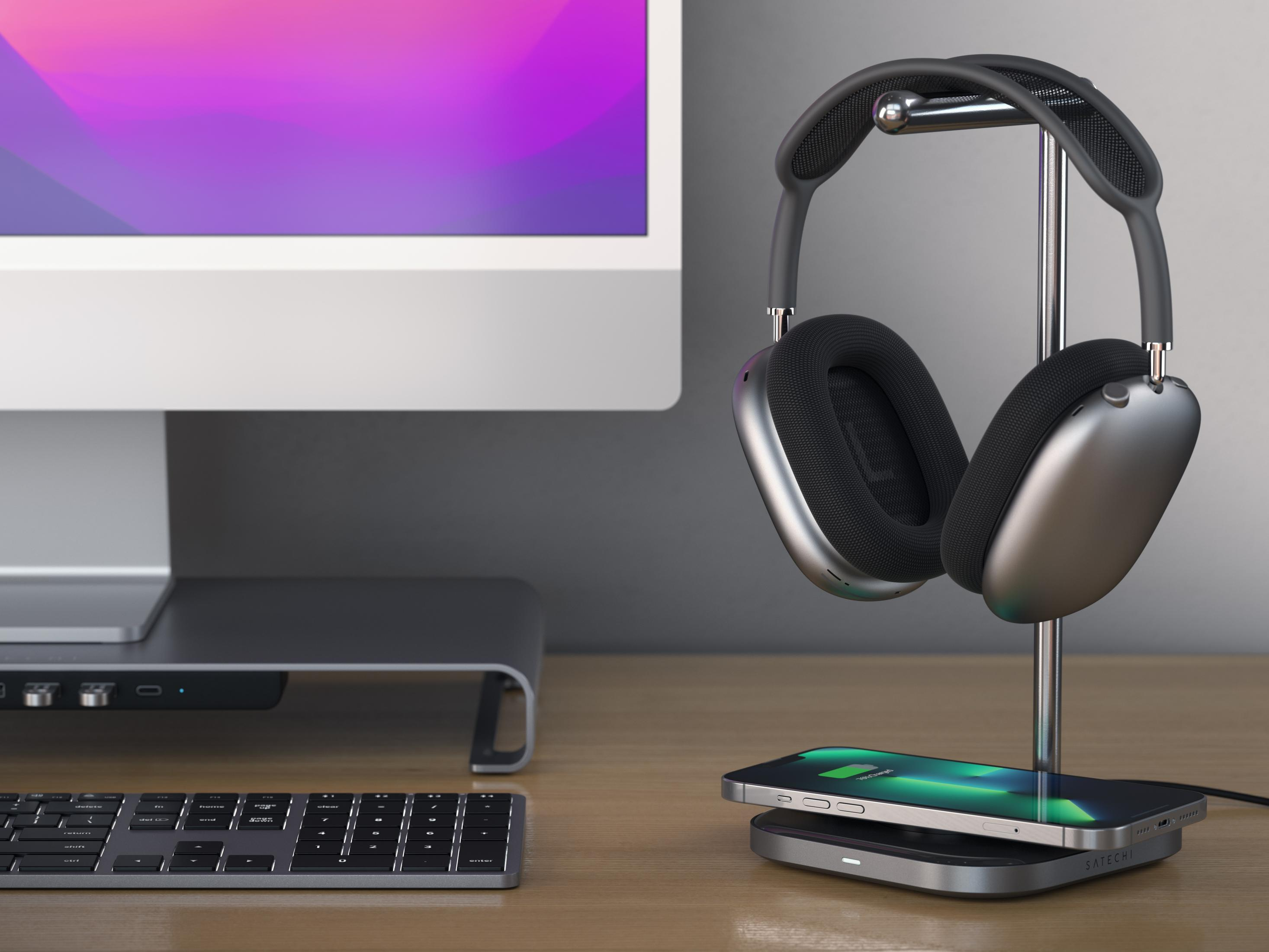 Cuffie su supporto, iPhone in carica su scrivania accanto al computer.
