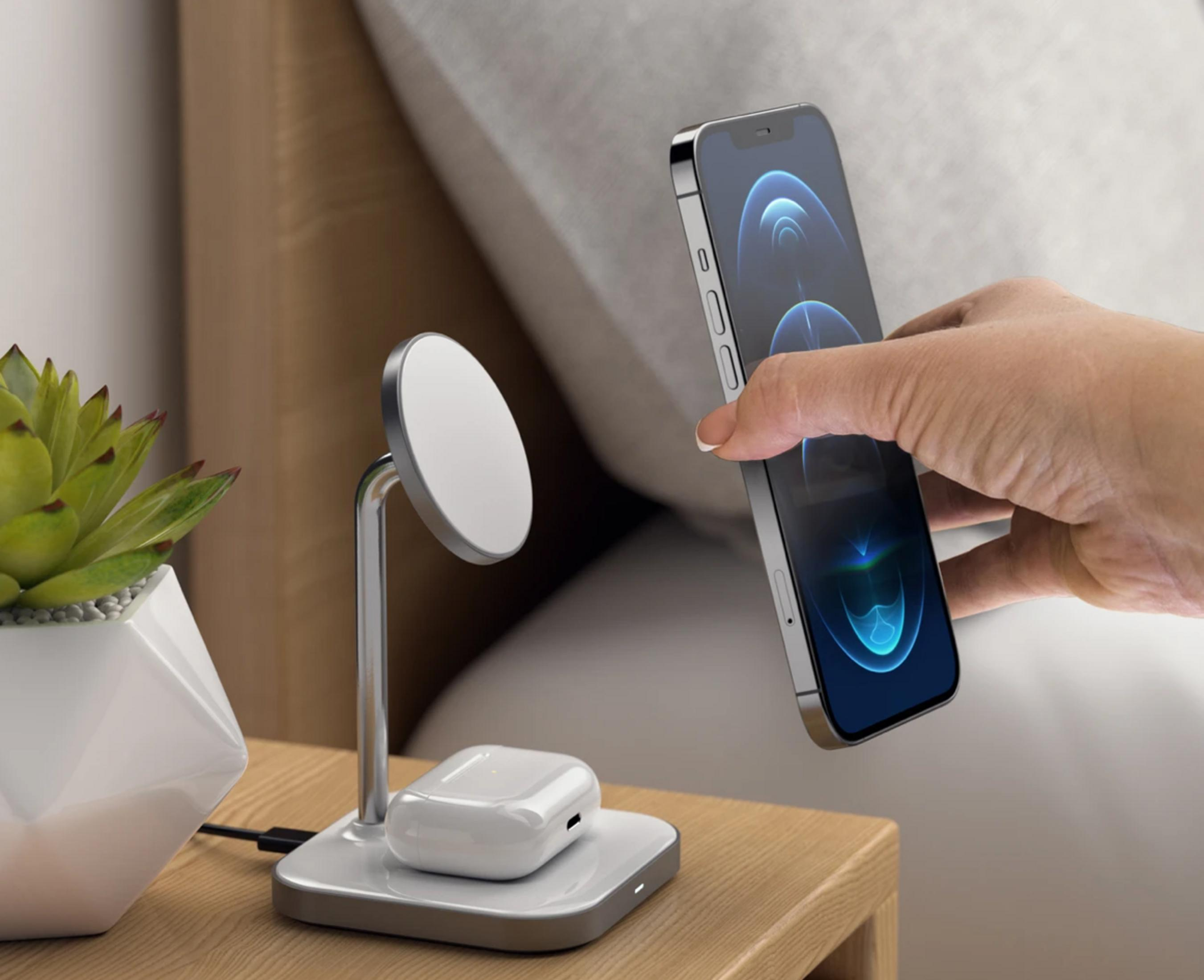 Un iPhone è tenuto sopra un caricabatterie, con AirPods e una pianta nelle vicinanze.