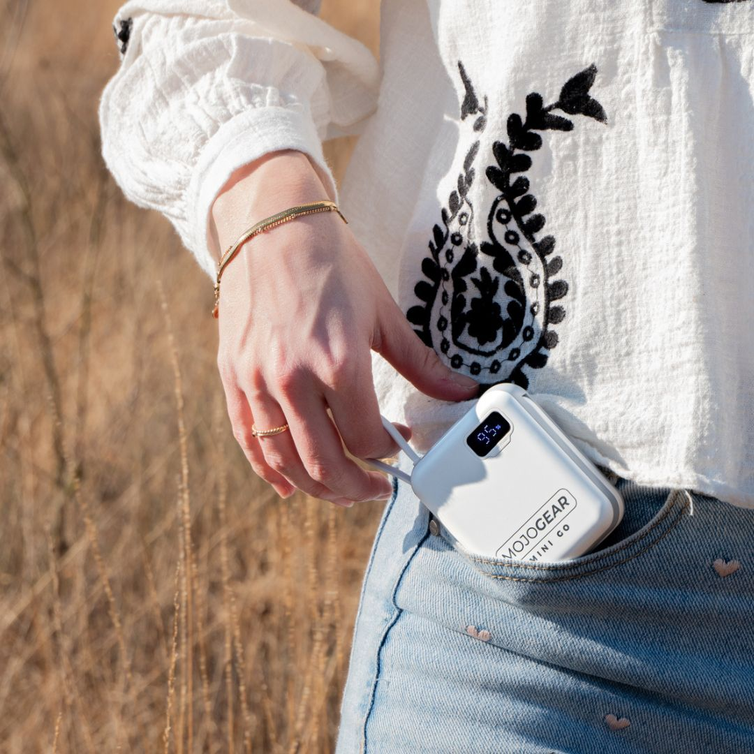 Eine Hand steckt eine weiße Powerbank mit digitaler Anzeige in eine Jeans-Hosentasche.