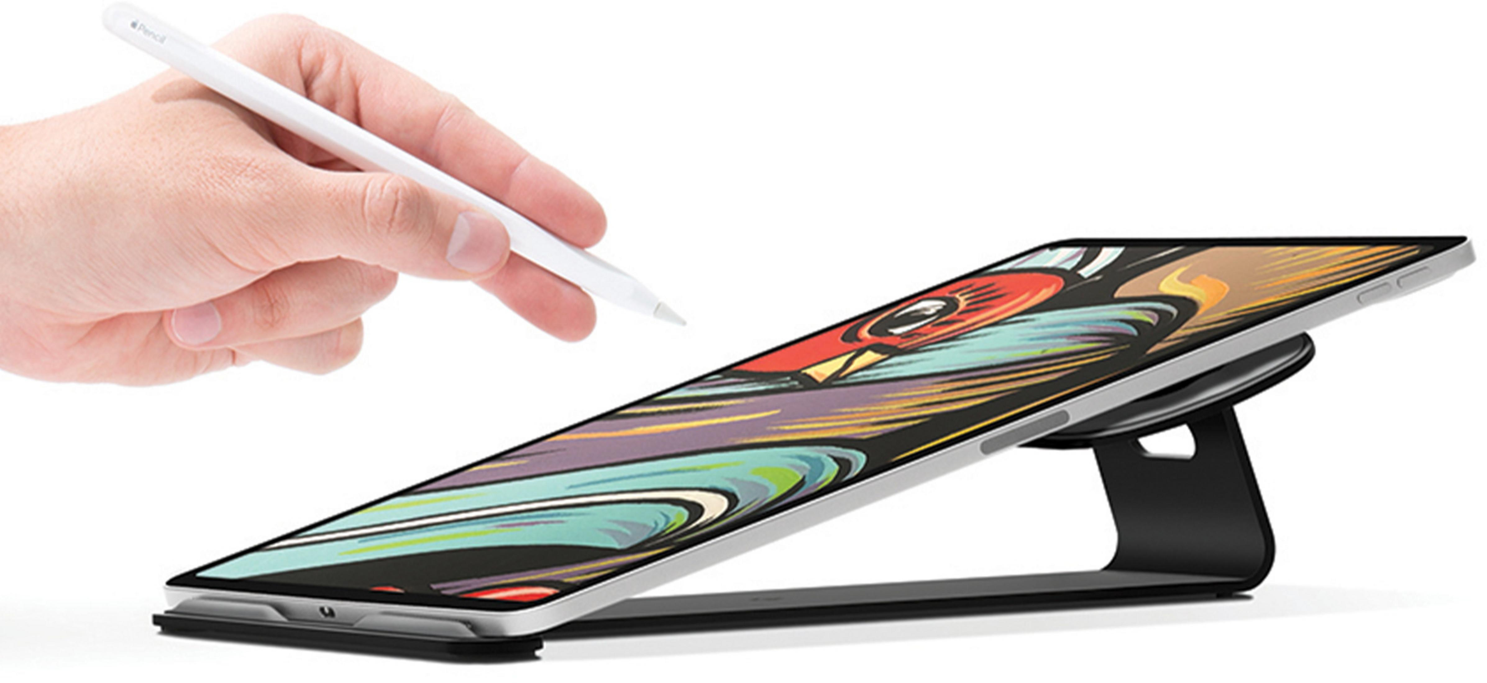 Une main tient un stylet blanc sur une tablette à écran coloré sur un support.