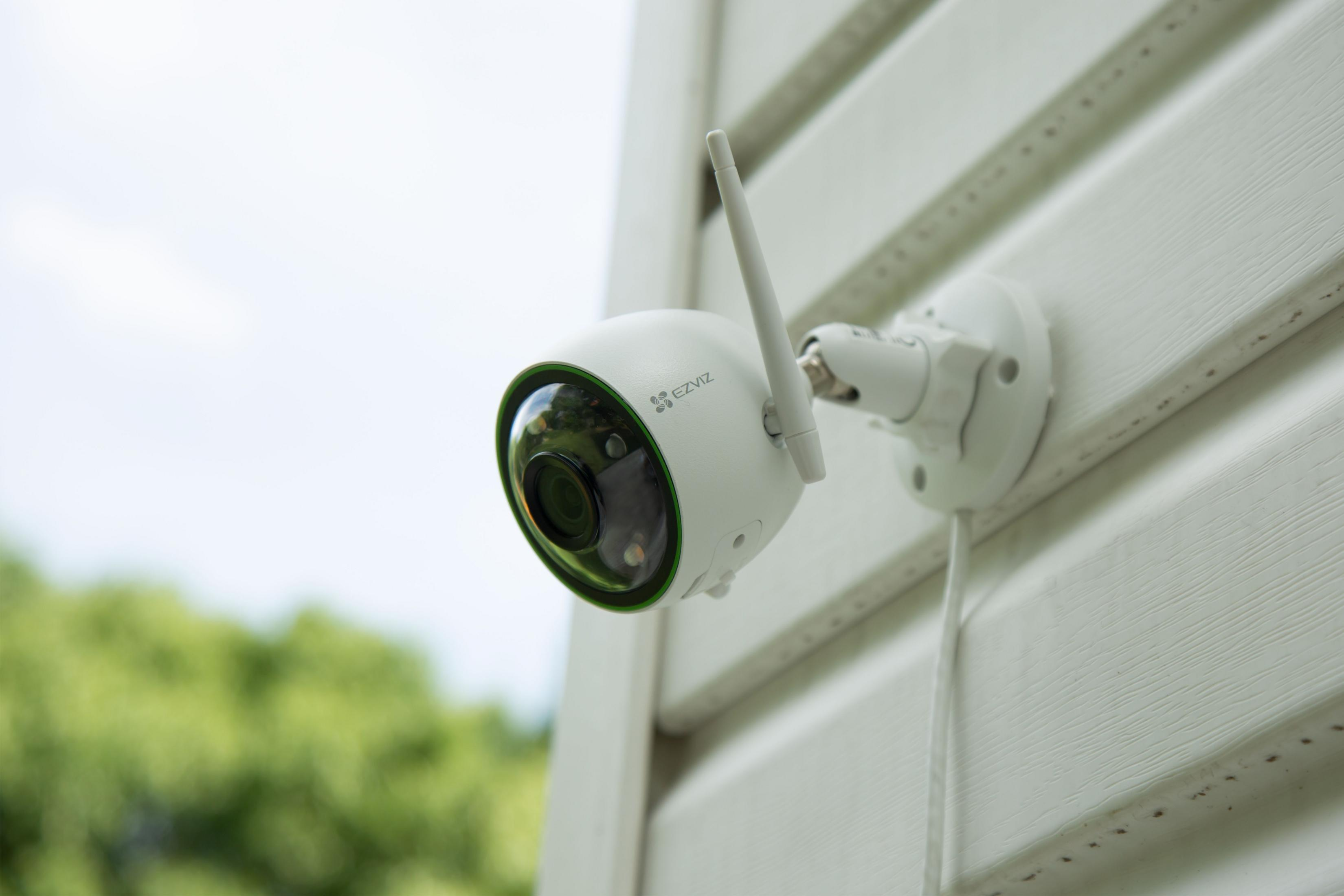 Una cámara de seguridad blanca con antena está montada en una pared blanca.