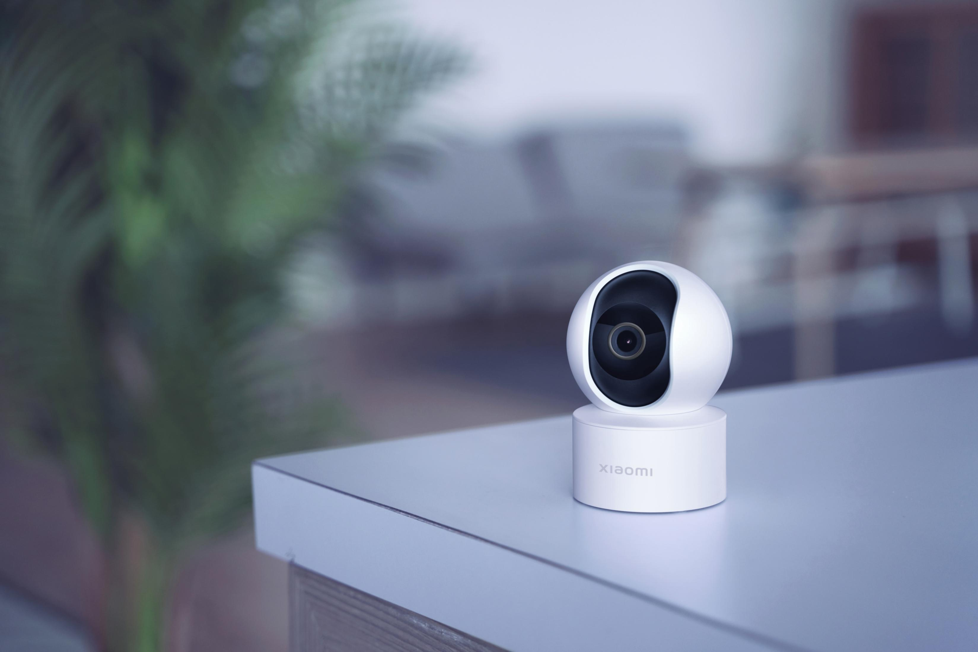 Biała kamera bezpieczeństwa Xiaomi stoi na stole z rozmytym zielonym tłem.